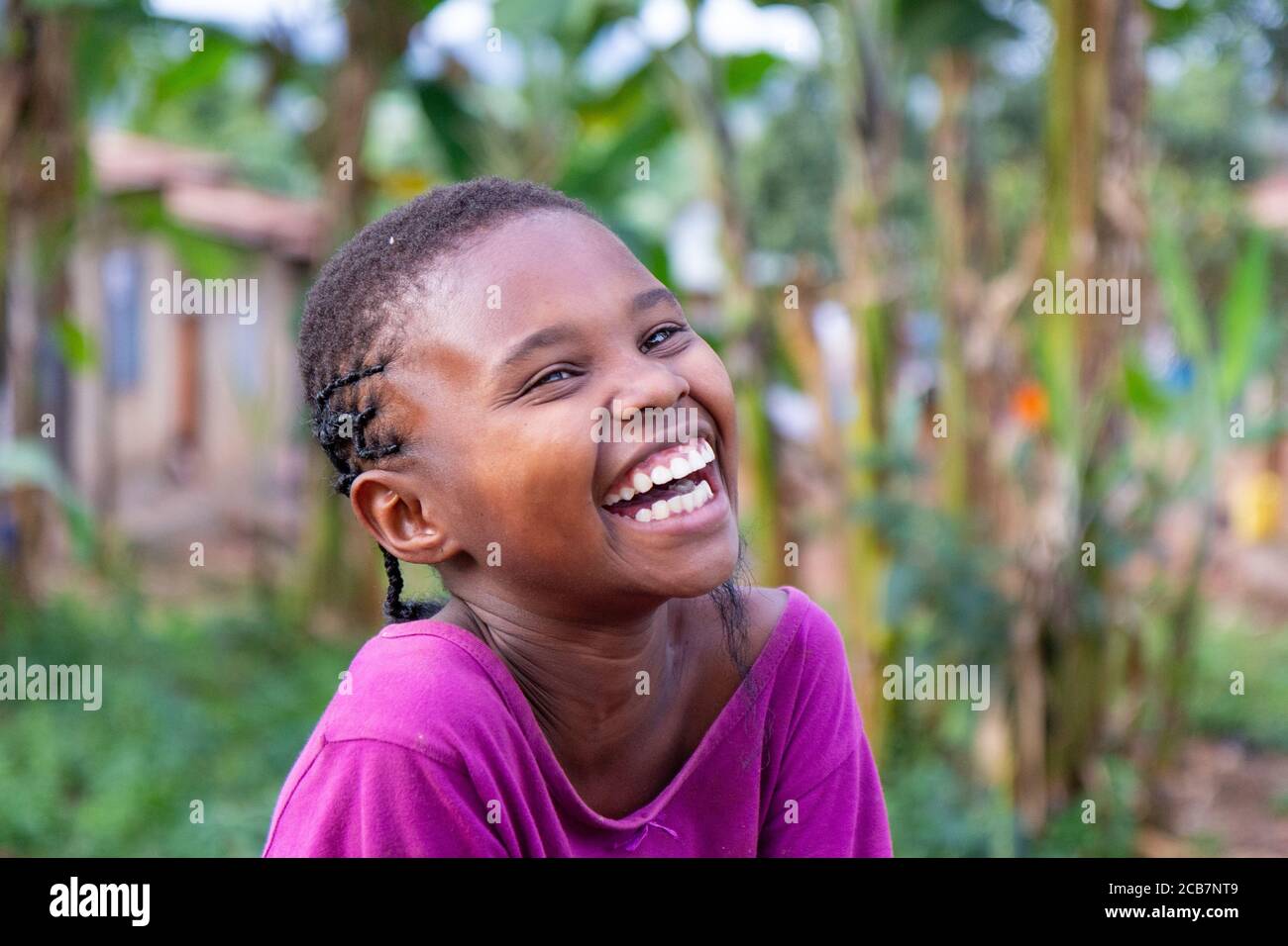 Une fille qui rit assise sur un tronc d'arbre tombé. Tourné en Ouganda en 2017. Banque D'Images