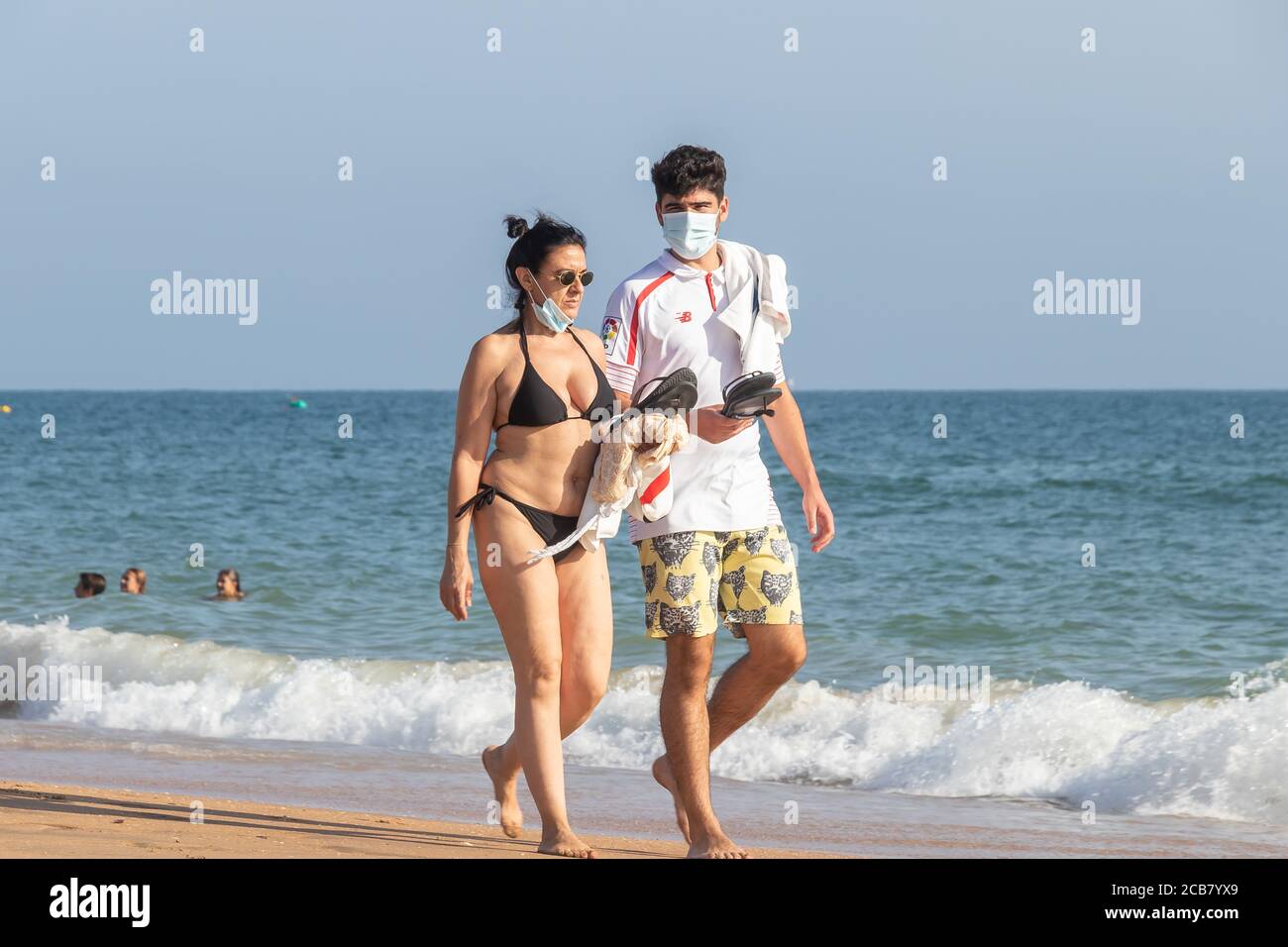 Punta Umbria, Huelva, Espagne - 7 août 2020 : couple marchant sur la plage en portant des masques protecteurs ou médicaux. Nouvelle normale en Espagne avec di social Banque D'Images