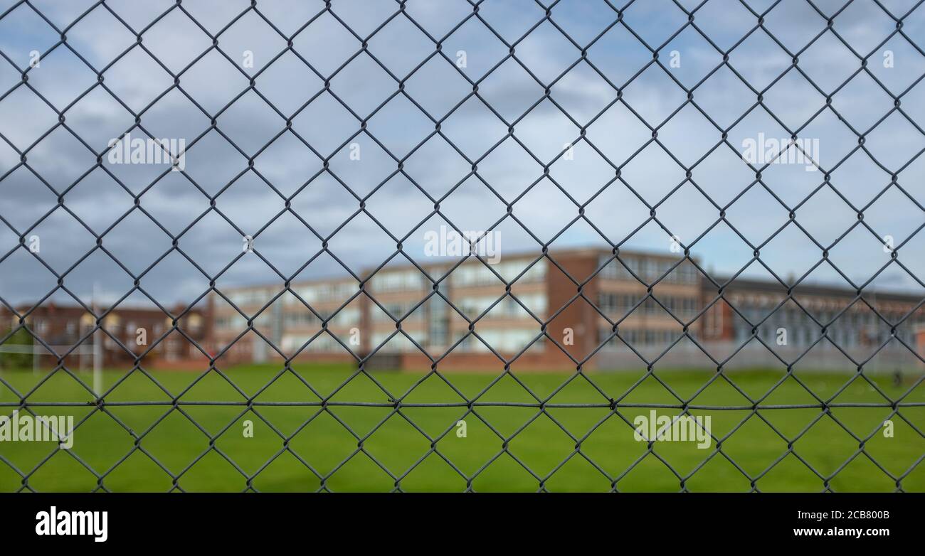 Un bâtiment de lycée typique et terrain de sport sous UN Ciel nuageux avec accent sur la clôture de sécurité dans le Premier plan Banque D'Images