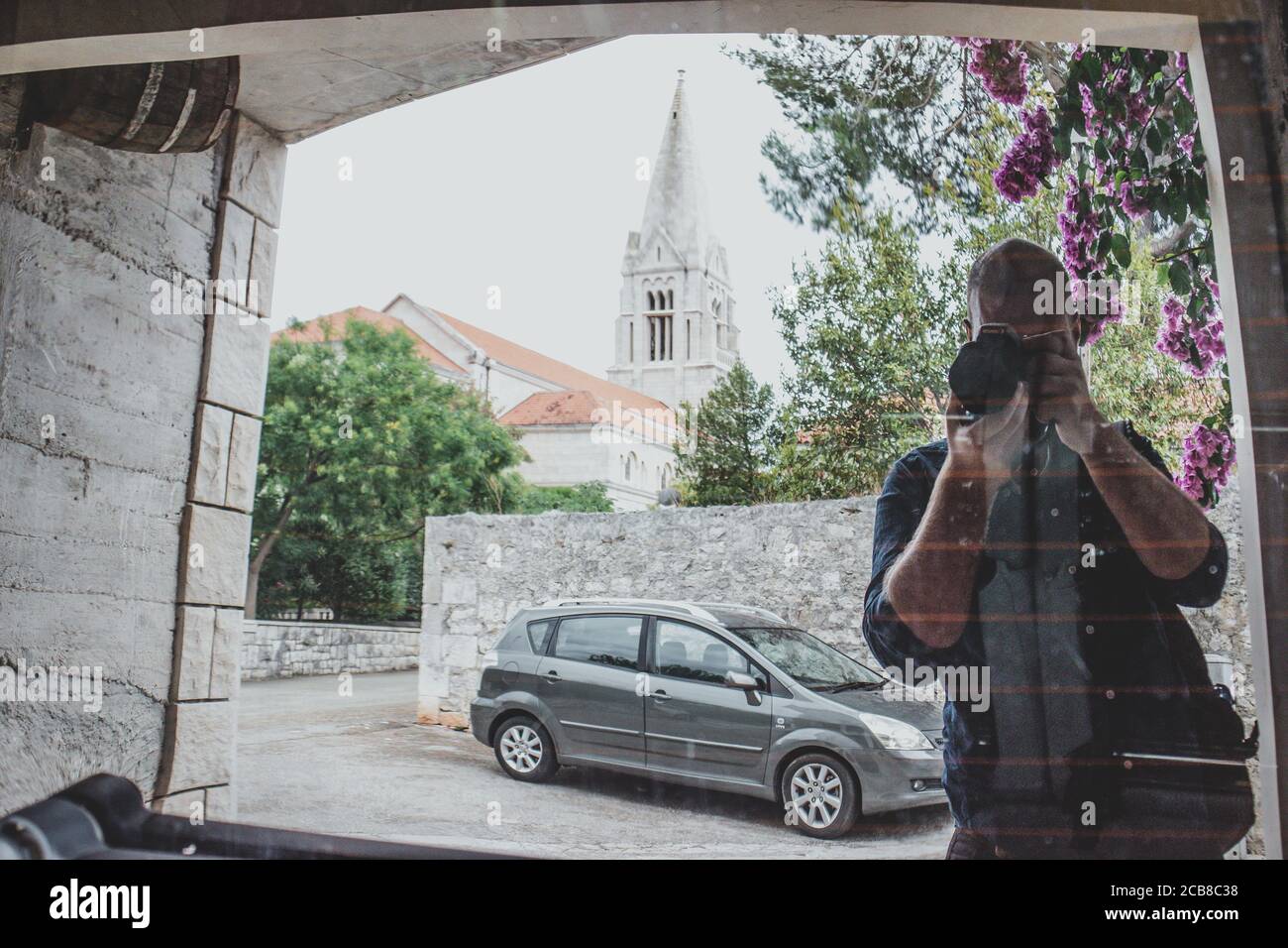 Homme prenant une photo de lui-même dans la résection d'une voiture fenêtre, église sur l'île de brac en croatie visible dans le reflet. Voyageur typique i Banque D'Images