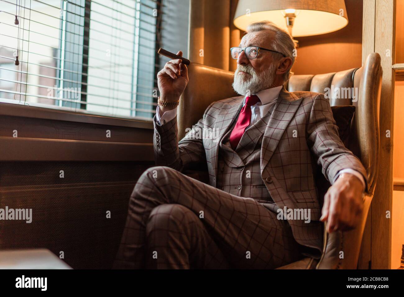 Vieux grave-aged businessman wearing classy adaptés sur mesure costume,  cravate rouge et coûteux à l'ancienne montre-bracelet sitting on sofa in  office, looking at Photo Stock - Alamy