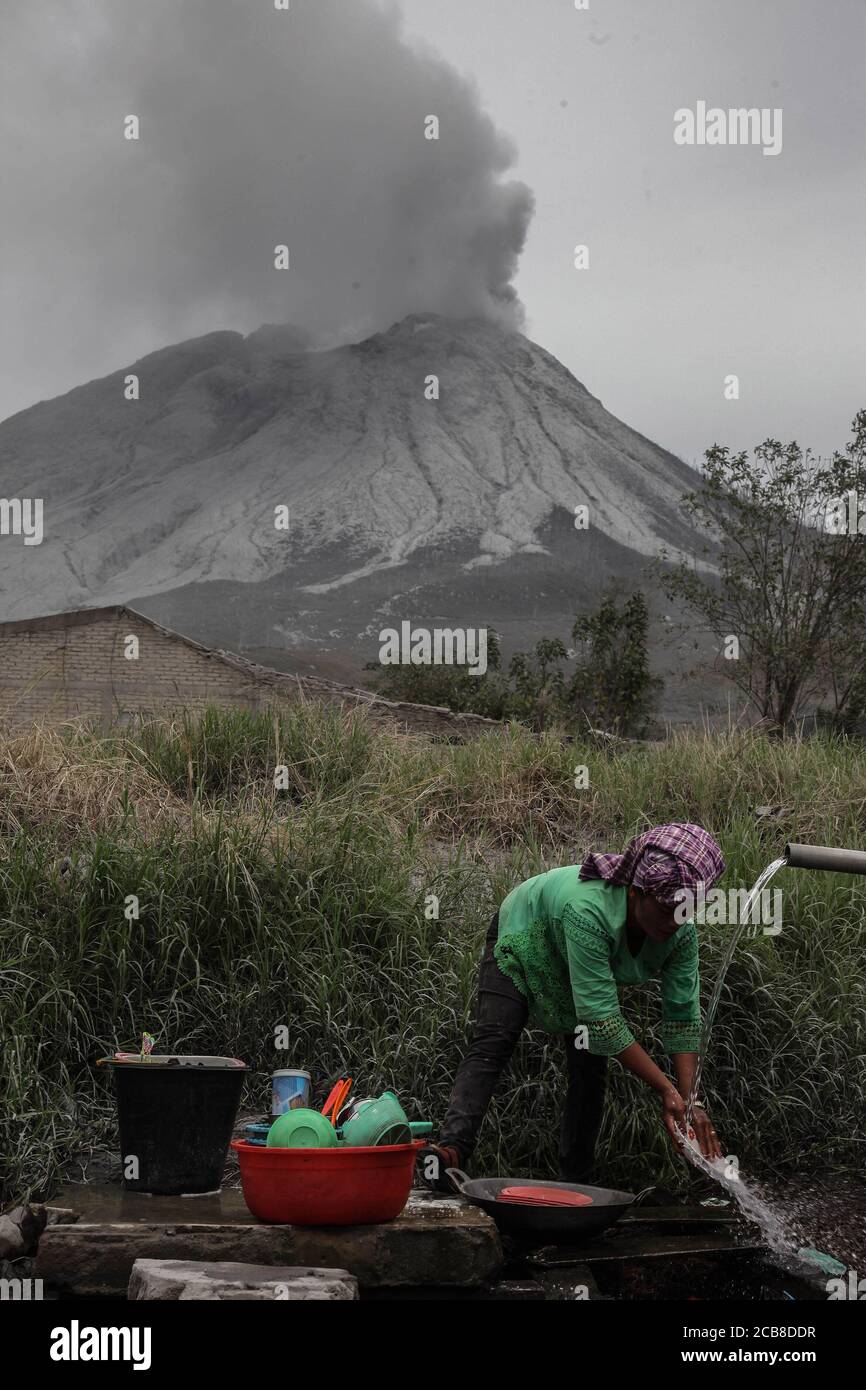 Karo, Sumatra Nord, Indonésie. 12 août 2020. Un villageois nettoie les cendres volcaniques de son équipement de cuisine au village de Naman Teran à Karo, au nord de Sumatra, le 11 août, 2020 un jour après l'éruption du mont Sinabung (arrière-plan) avec la hauteur de la colonne de cendres a été observée à environ 5,000 mètres au-dessus du pic ou à environ 7,460 mètres au-dessus du niveau de la mer. Les récoltes ont échoué en raison de l'épaisse cendre volcanique qui a couvert la zone. Crédit: Albert Ivan Damanik/ZUMA Wire/Alay Live News Banque D'Images