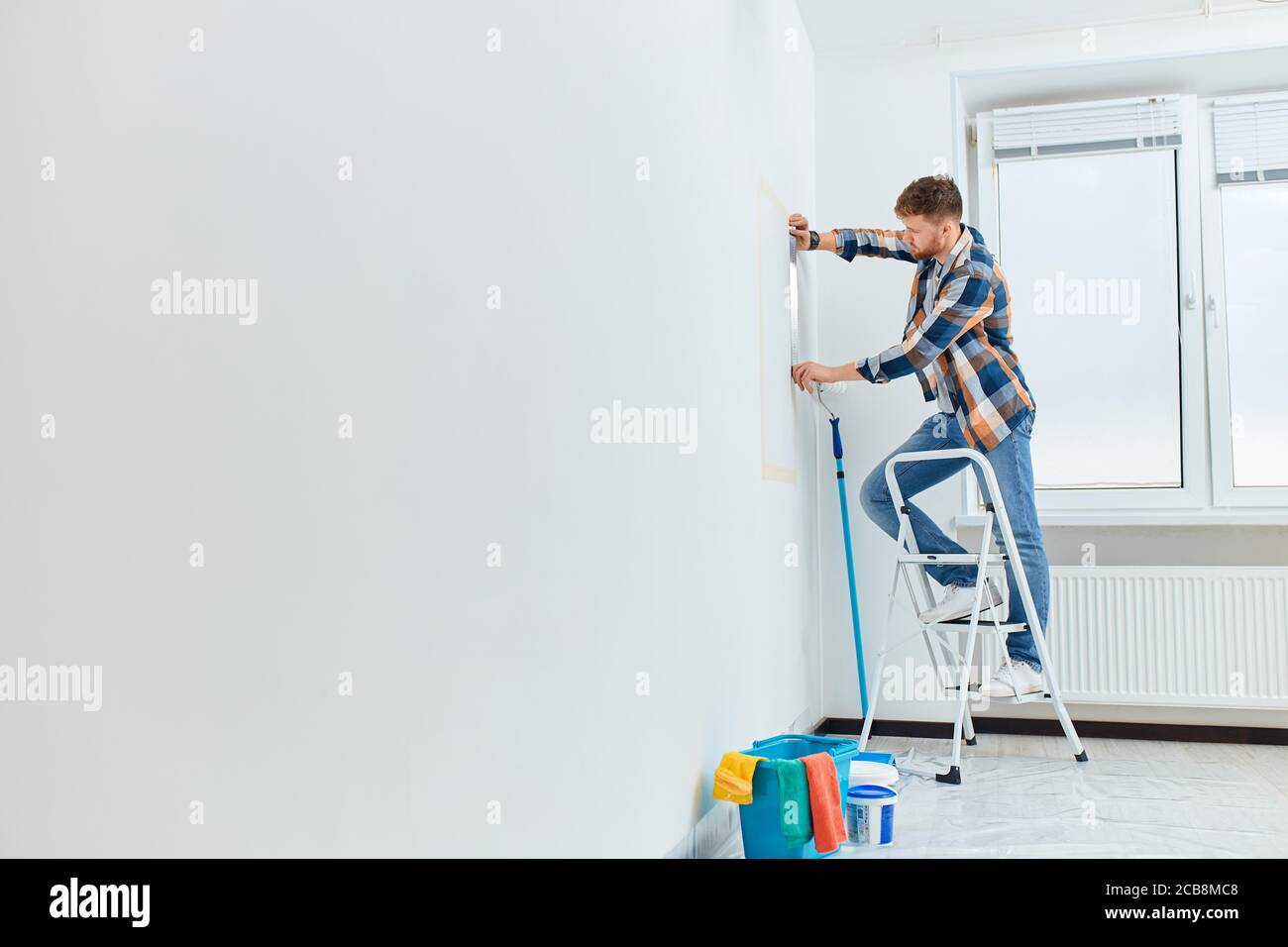 Mur de mesure d'architecte ou d'interio avec règle flexible debout sur une échelle dans un appartement blanc vide Banque D'Images