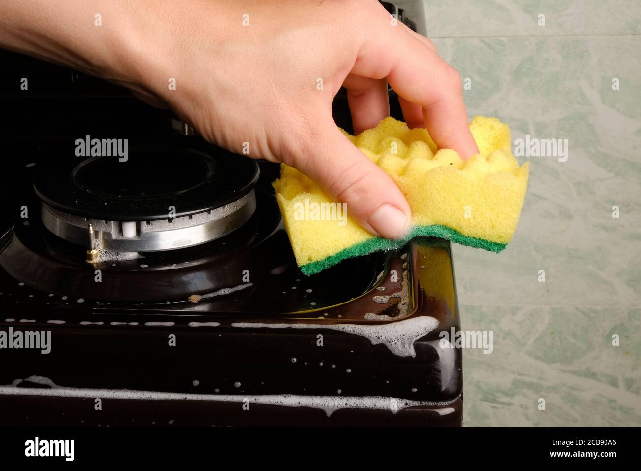 La main féminine nettoie le poêle à gaz avec une éponge avec de la mousse blanche, le nettoyage de la surface. Hygiène à la maison, les appareils. Banque D'Images