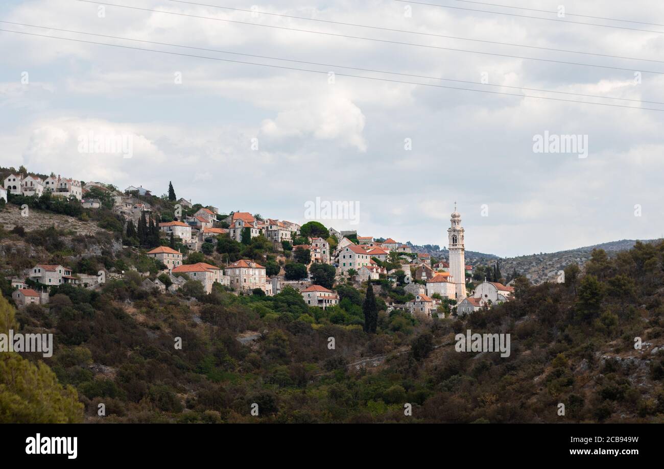 Grand clocher dans un petit village de Lozisca sur l'île de Brac, Croatie. Belle tour chrétienne s'élevant au-dessus des anciens bâtiments Banque D'Images