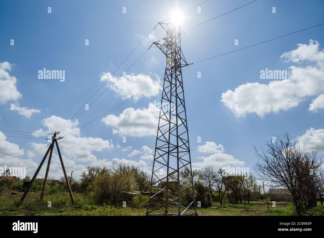 Une tour haute tension en métal contre un ciel bleu avec des nuages blancs qui s'élèvent au-dessus des arbres. Alimentation Banque D'Images