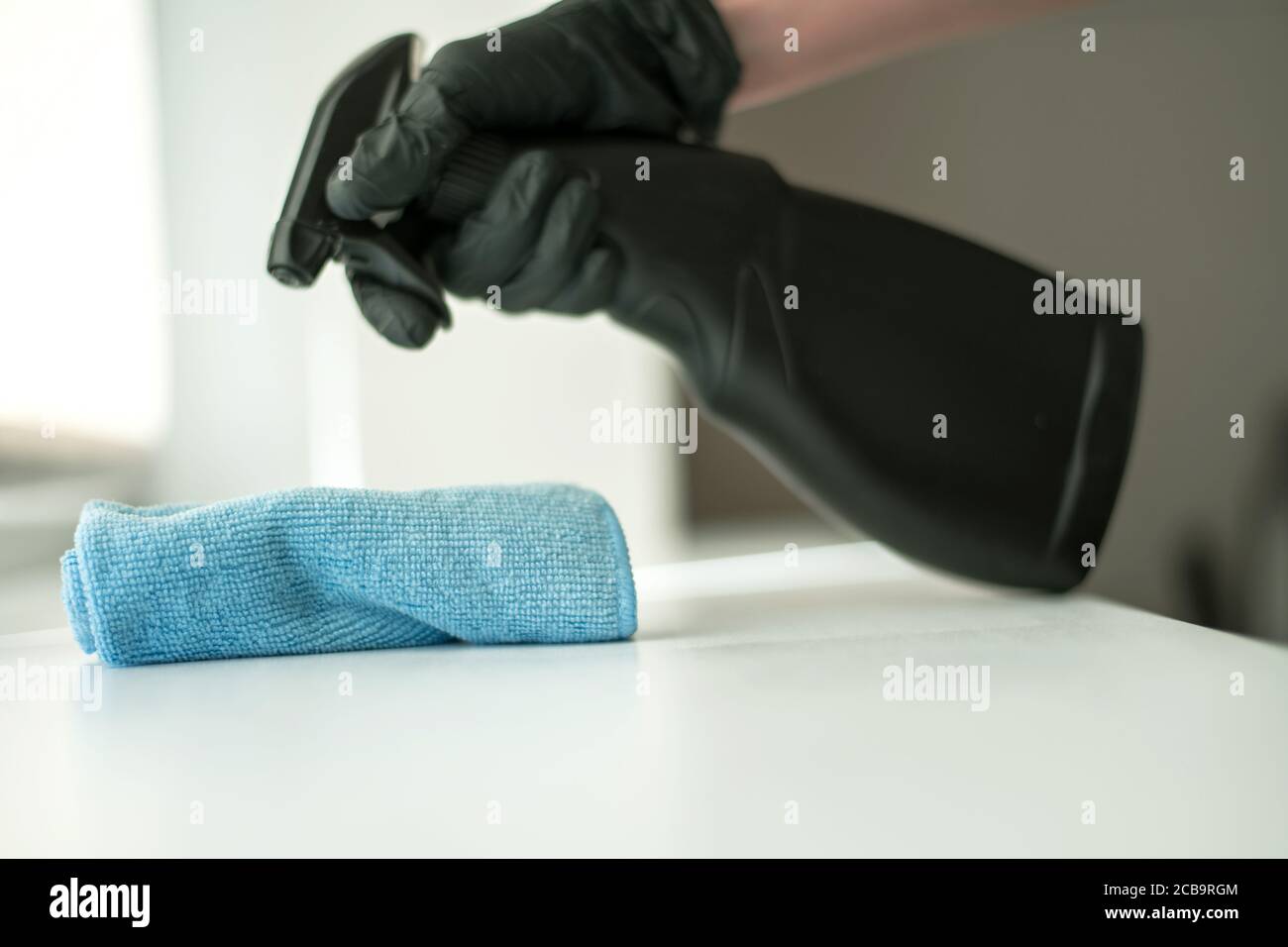 Une main dans des gants noirs tient un chiffon de nettoyage en microfibre et un spray avec stérilisation font la désinfection pour une bonne hygiène Banque D'Images