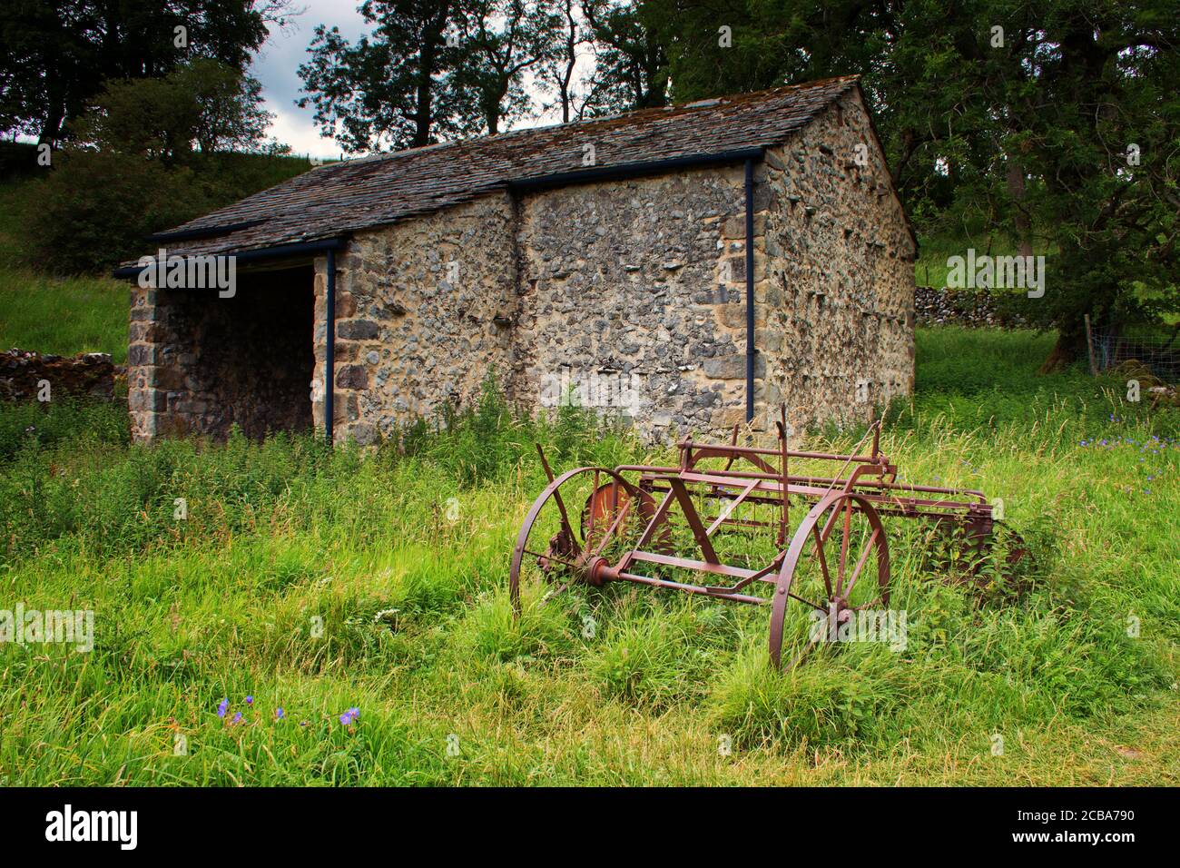Vieux matériel agricole installé en face d'une ancienne grange à Malham, Yorkshire Dales Banque D'Images