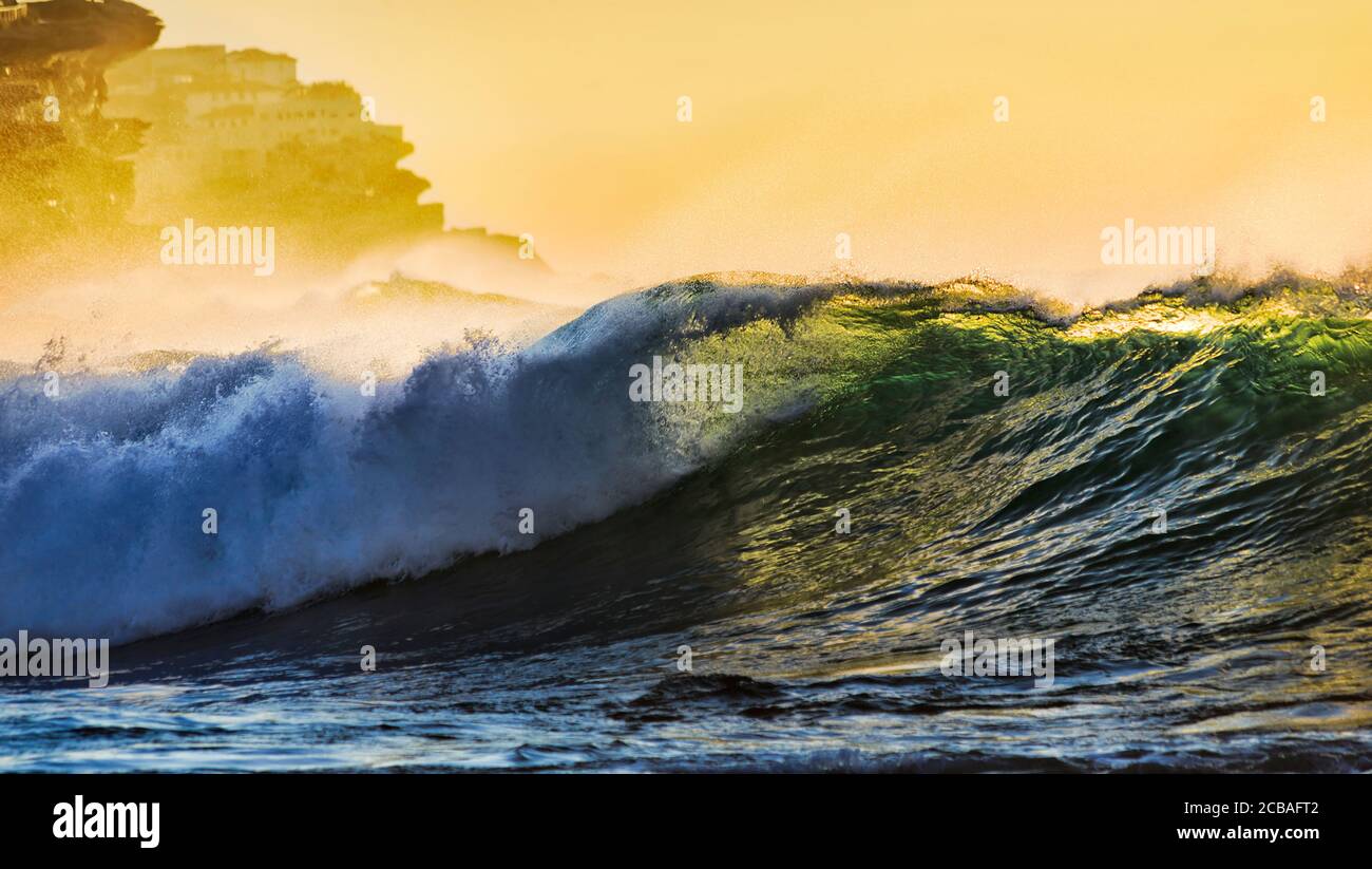 Vague d'émeraude se déroulant sur la plage de Bronte, dans la banlieue est de Sydney, sur la côte du Pacifique, au lever du soleil, autour des falaises de grès. Banque D'Images