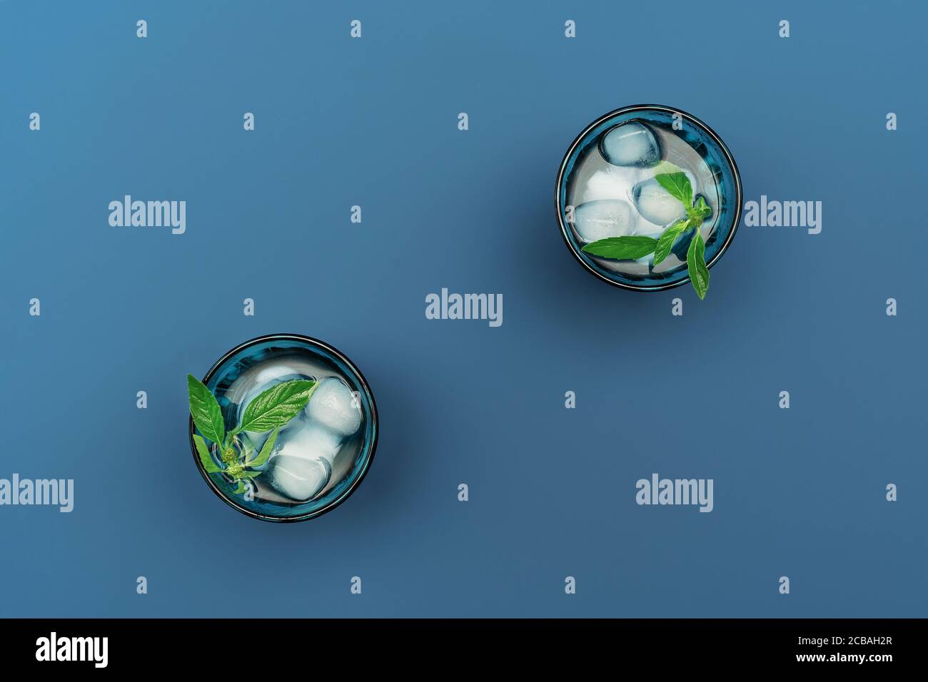 Deux magnifiques verres bleus vintage avec boisson froide et glaçons, avec feuilles de menthe verte fraîche sur fond bleu profond. Toile de fond pour votre conception. Style de pose à plat. Banque D'Images