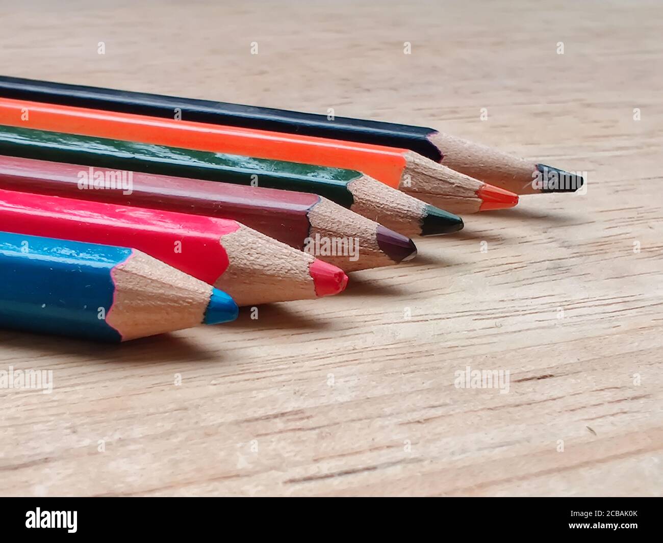Résumé plat / disposition avec crayons de couleur aiguisés placés sur une planche en bois. Les couleurs bleu, rouge, orange, vert, noir sont visibles ici Banque D'Images
