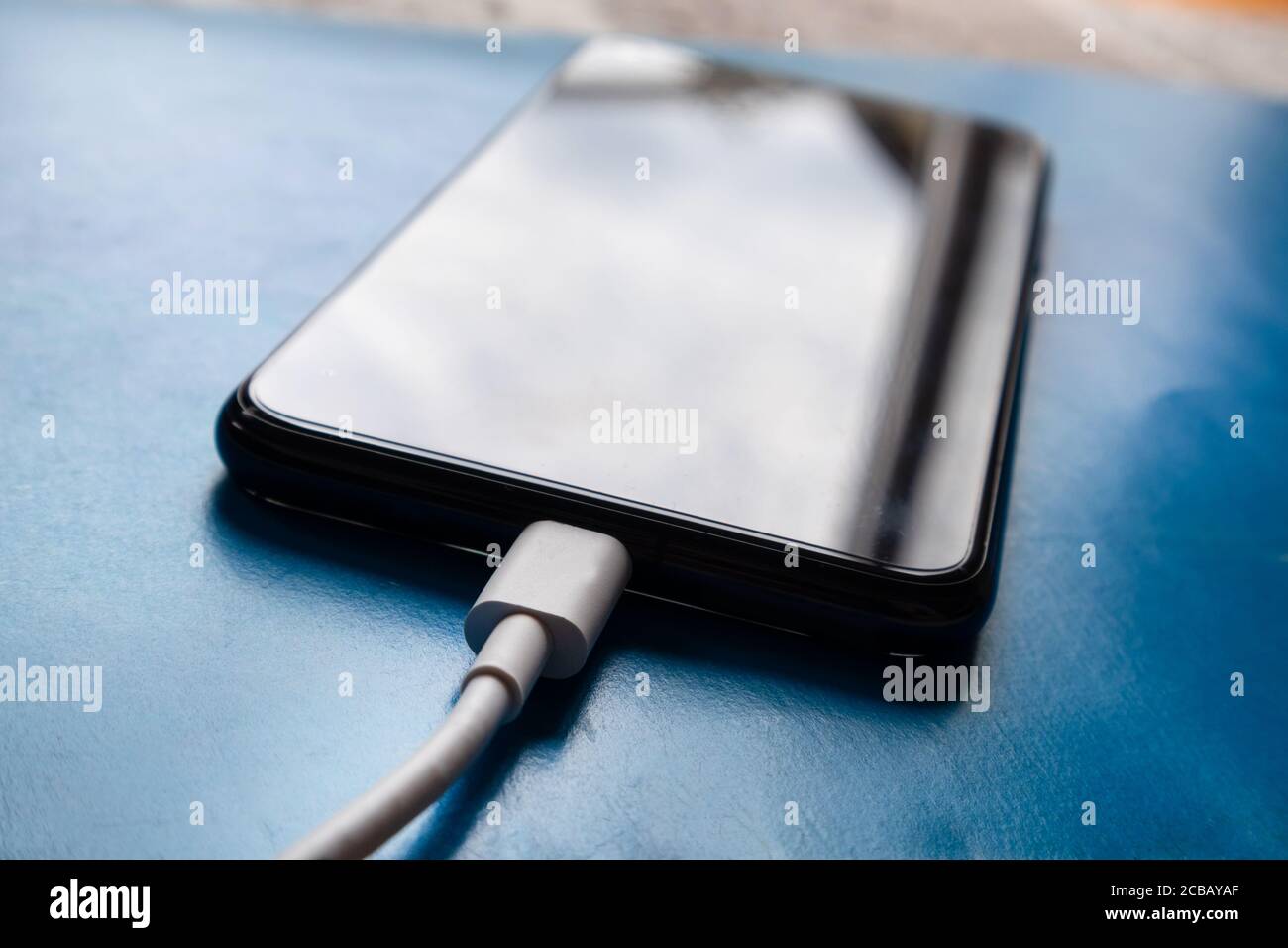 Câble de chargement de téléphone blanc branché à un smartphone sur un bureau bleu à la maison. Technologie intelligente et concept de charge Banque D'Images