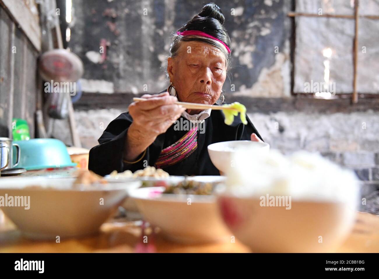 (200812) -- NINGDE, le 12 août 2020 (Xinhua) -- Zhong Lianjiao Dines à la maison au village de Banyueli dans le comté de Xiapu, dans la province de Fujian du sud-est de la Chine, le 5 août 2020. Il est courant de voir Zhong Lianjiao, une femme de 89 ans du groupe ethnique She toujours dans les costumes traditionnels She, présenter les cultures de son groupe ethnique aux touristes visitant l'ancien village Banyueli. Vivant dans le village depuis des décennies, Zhong s'efforce de promouvoir le tourisme du village en introduisant les cultures locales aux touristes. Banyueli est un village où les reliques culturelles et les coutumes folkloriques de son groupe ethnique Banque D'Images