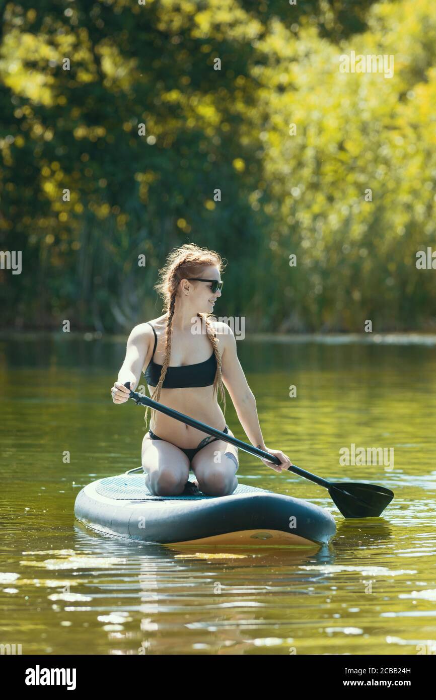 Rafting - jeune femme en maillot de bain noir assise sur un radeau de natation et aviron avec un ramon. Mid shot Banque D'Images