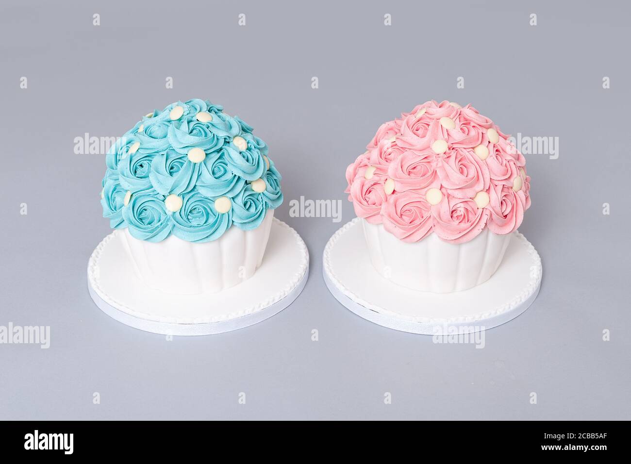 Deux cupcake géant Victoria maison avec des tourbillons de crème au beurre rose et bleu et des boutons de chocolat blanc sur le dessus pour décorer avec garniture de confiture et Banque D'Images