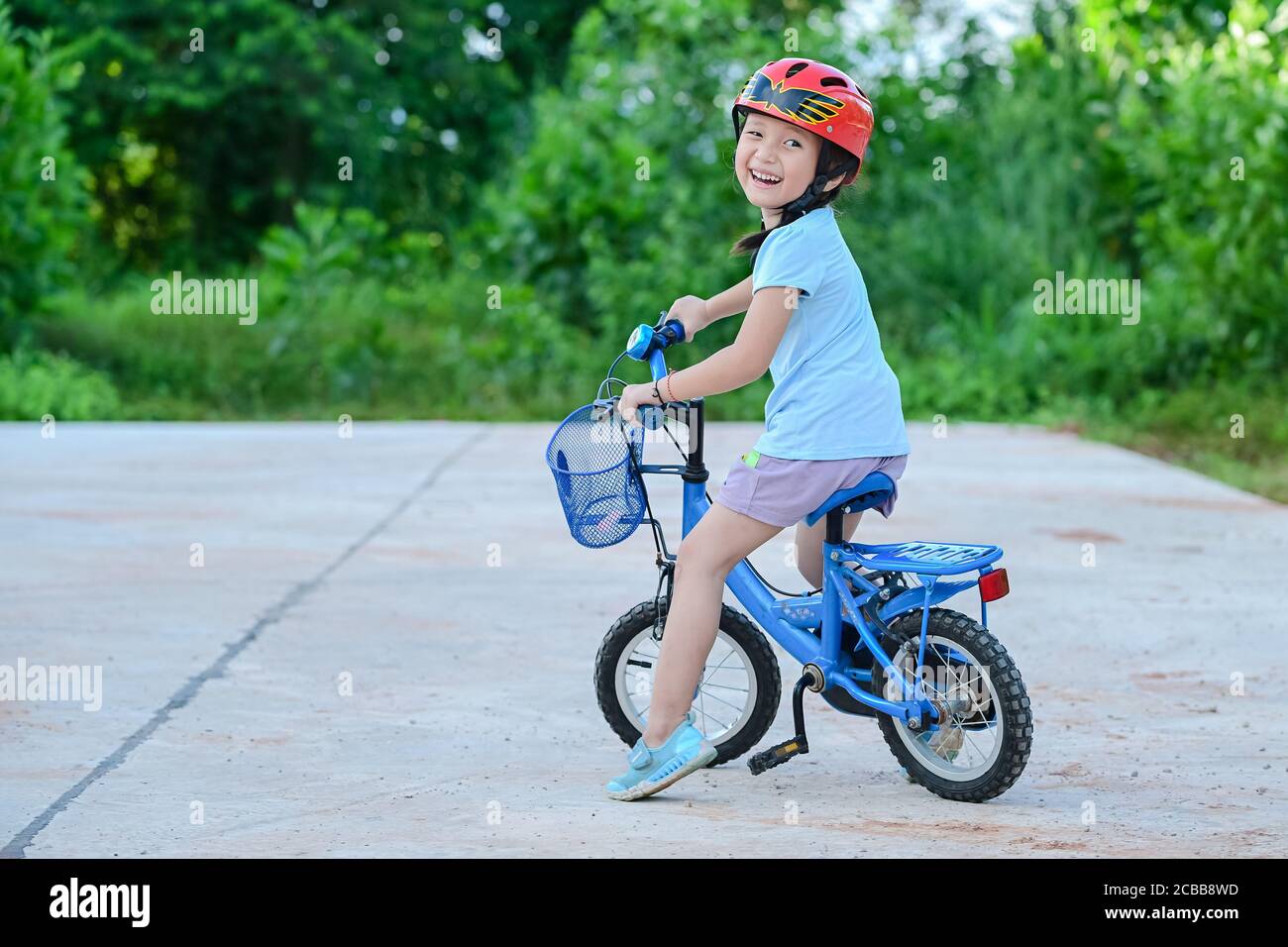Bonne fille à vélo dans le parc de jardin . Enfant actif portant un casque de vélo. Sécurité sports loisirs avec concept enfants Banque D'Images