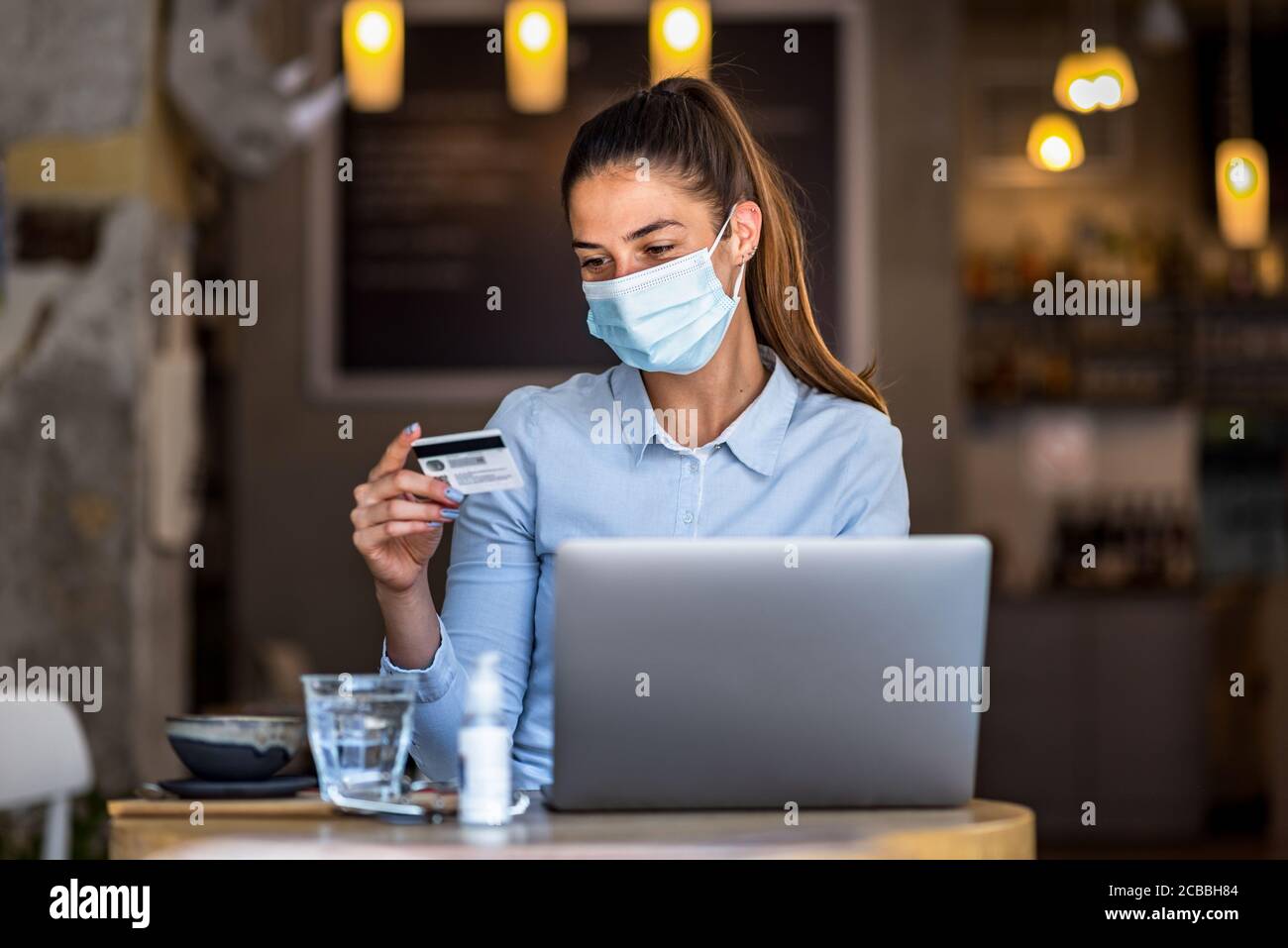 Portrait de jeune femme d'affaires portant un masque tout en faisant des achats en ligne et le paiement par cartes de crédit. Nouveau mode de vie normal pendant la pandémie de Covid-19. Banque D'Images
