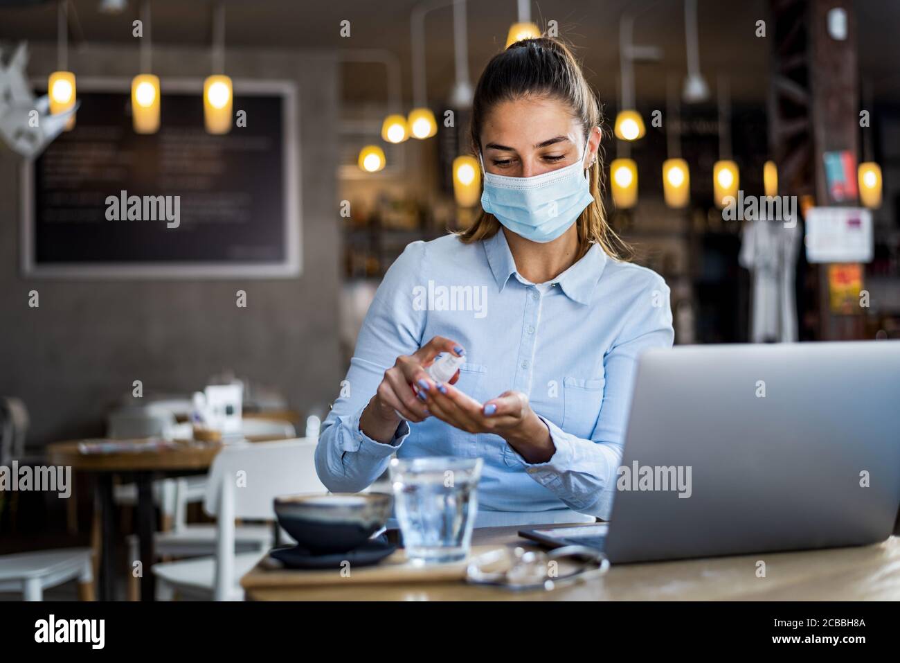 Portrait d'une jeune femme avec masque chirurgical en utilisant du gel désinfectant pour les mains au restaurant. Antiseptique, virus pandémique Corona, concept d'hygiène et de soins de santé. Banque D'Images