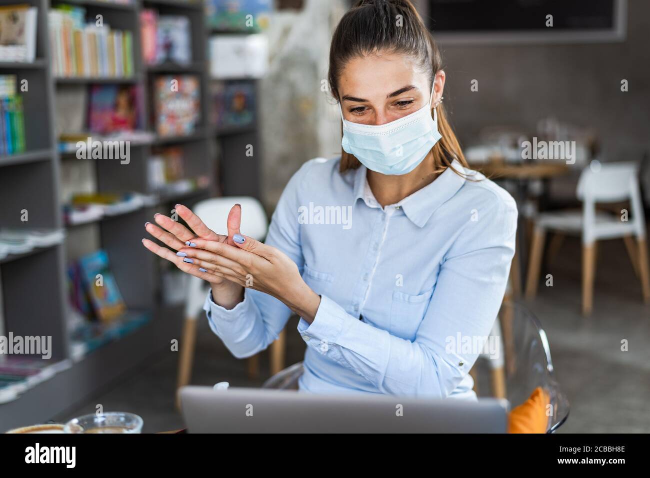 Portrait d'une jeune femme avec masque chirurgical en utilisant du gel désinfectant pour les mains au restaurant. Antiseptique, virus pandémique Corona, concept d'hygiène et de soins de santé. Banque D'Images