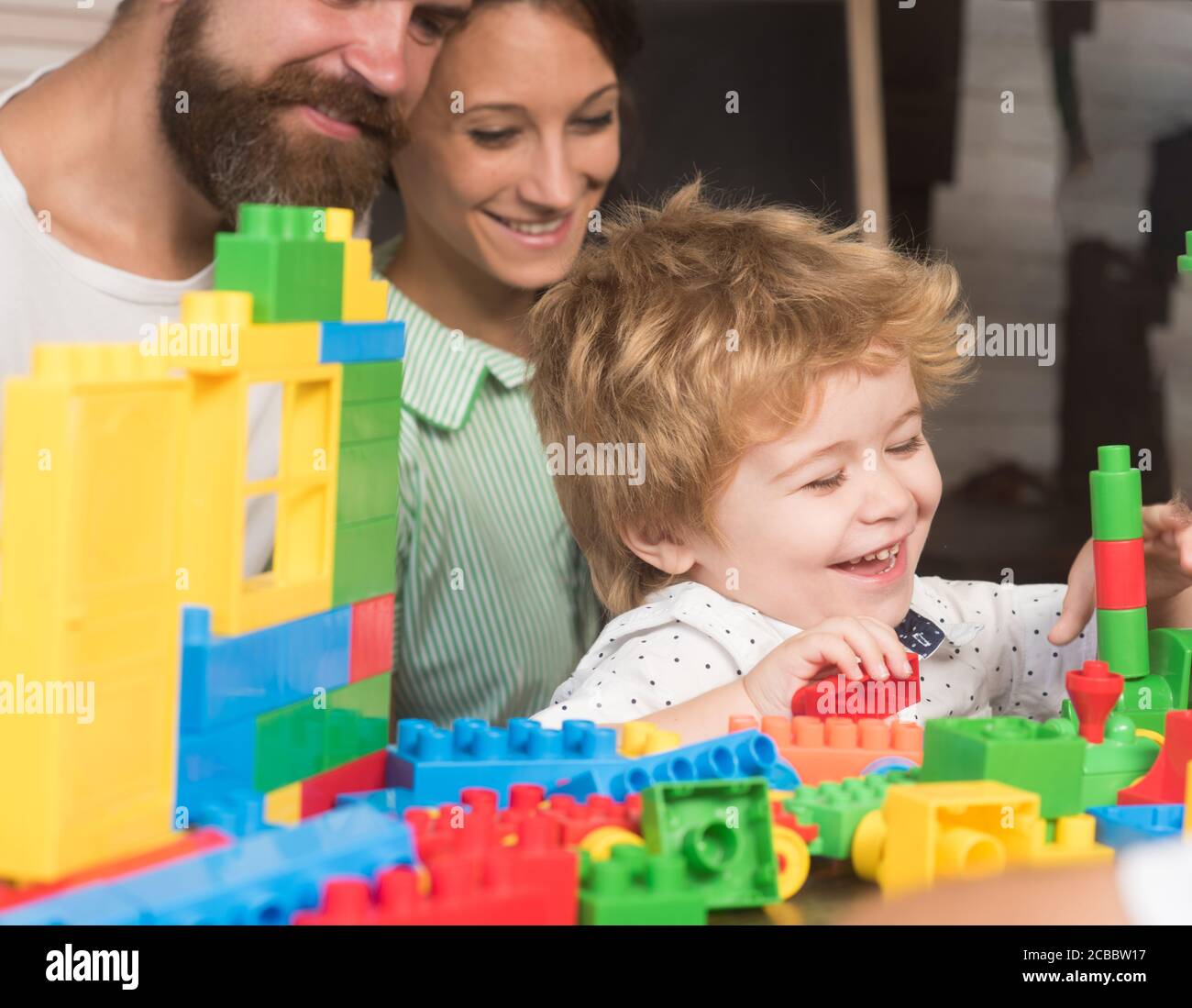 Bebe Garcon Regarde Un Jouet Fait De Blocs De Construction Enfant Avec Visage Souriant Pres Des Parents Dans La Salle De Jeux Sur Fond Defoque Concept De Jeux Familiaux Enfant Joue Avec