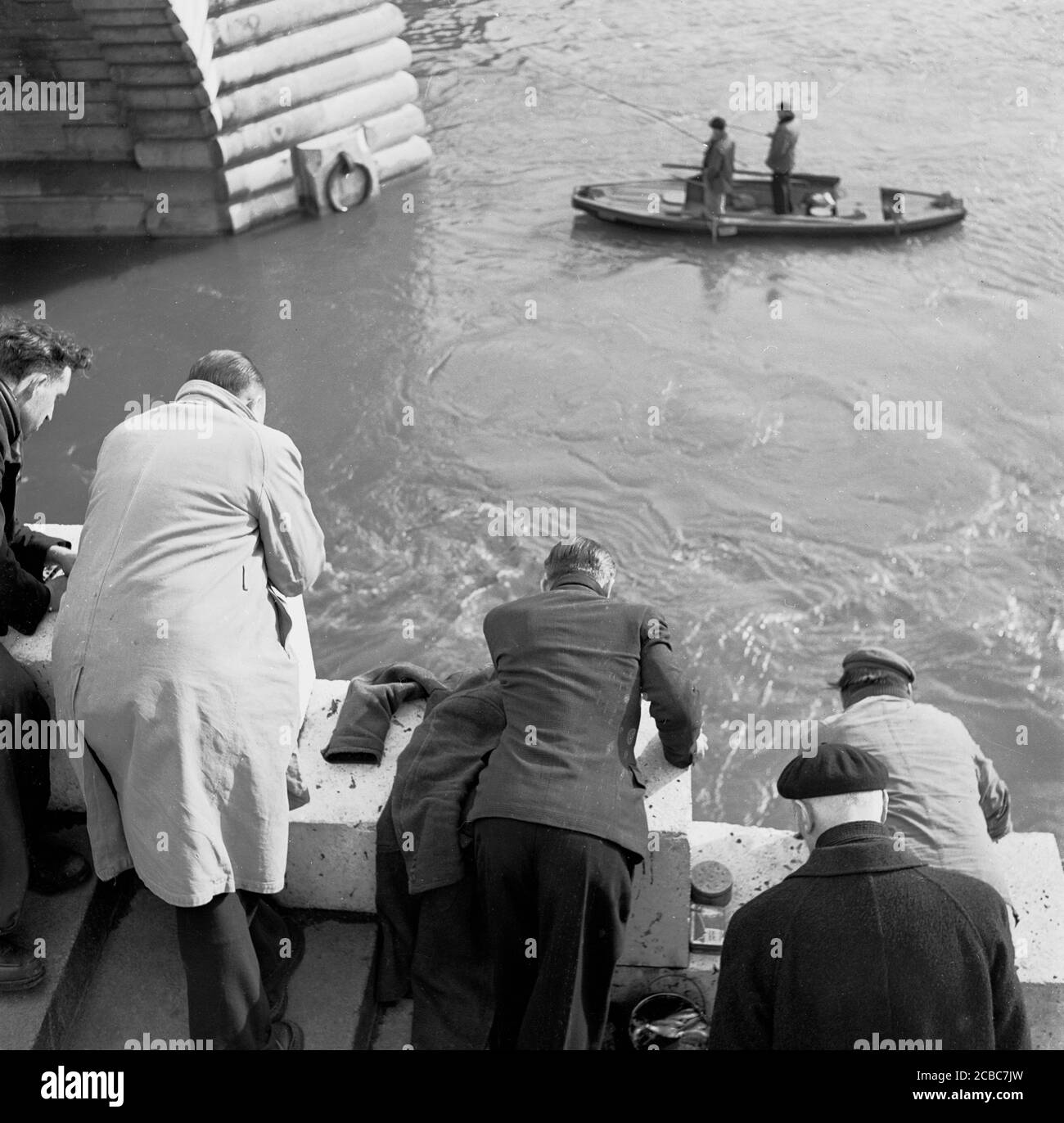 Années 1950, historique, Paris, France, pêcheurs parisiens regardant sur la Seine. Un bateau à rames dans la rivière avec des hommes de pêche peut également être vu. Banque D'Images