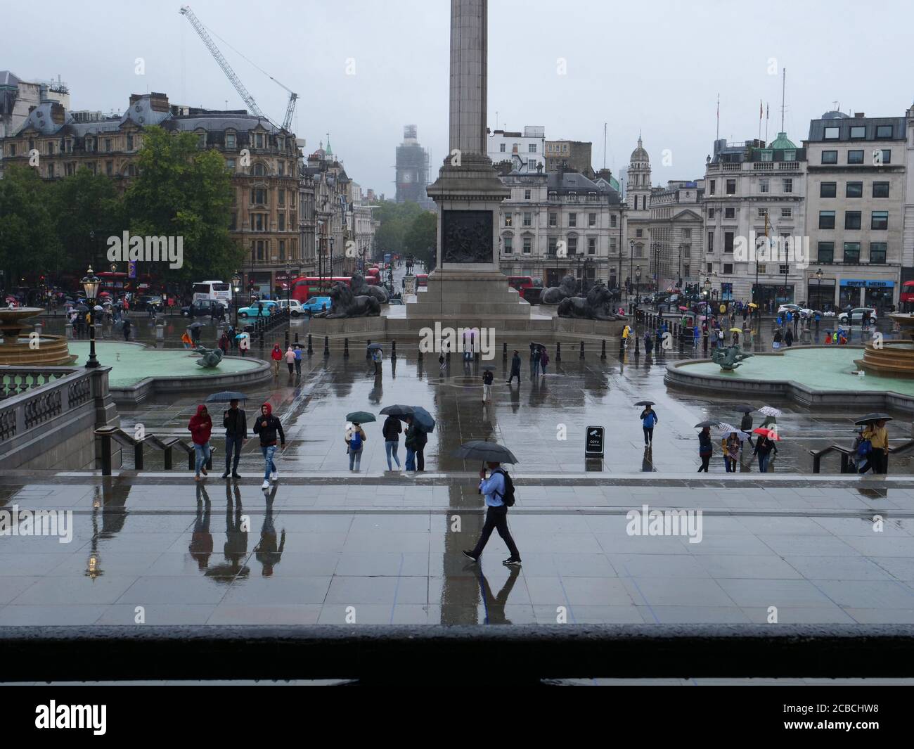 Vue générale des touristes vus marcher avec des parasols sur Trafalgar Square, Londres, un jour pluvieux en août. Banque D'Images