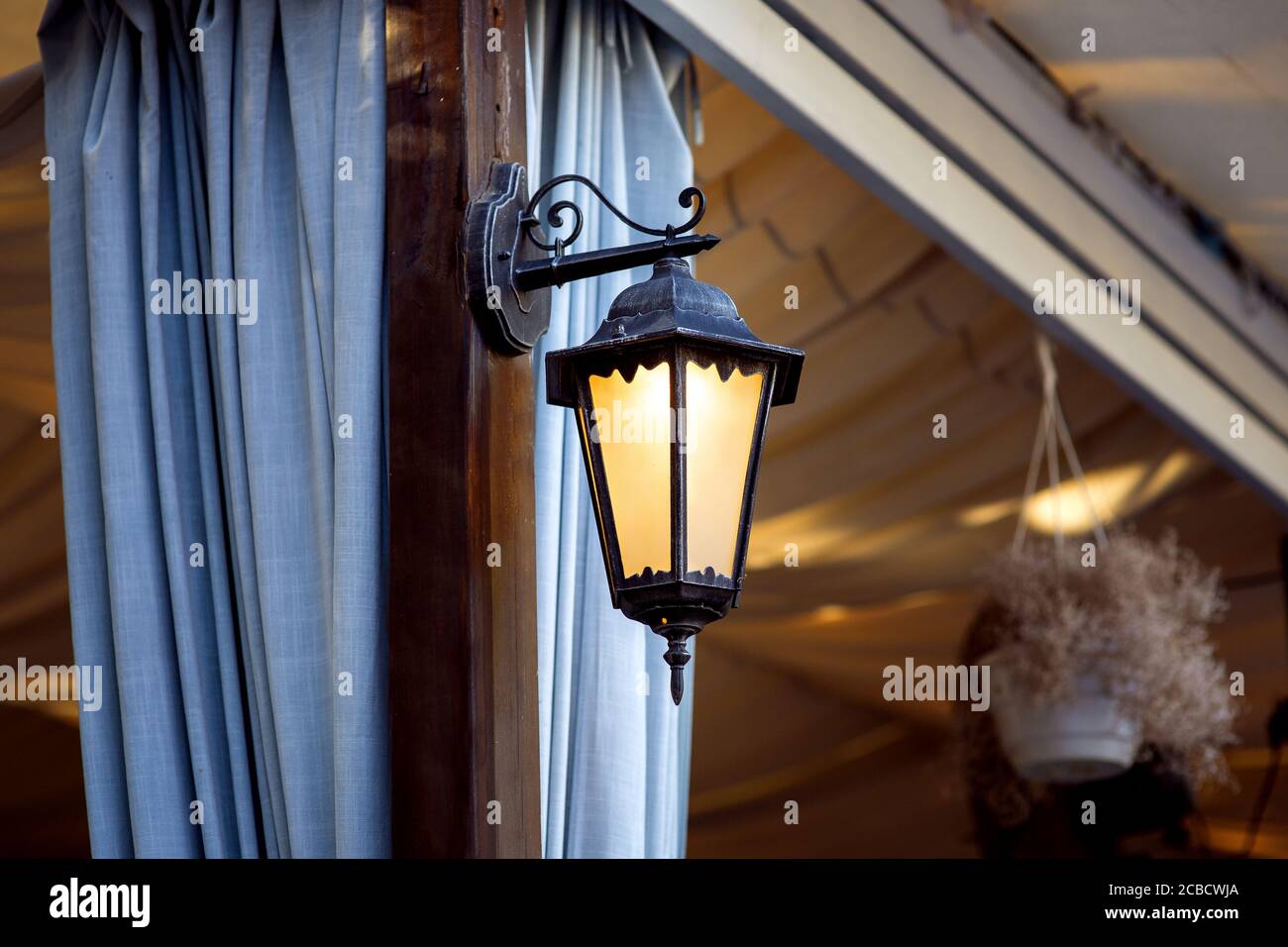 lanterne décorative pour belvédères et terrasses en fer forgé, sconces sur un pilier brun avec des rideaux bleus pesant des plis. Banque D'Images