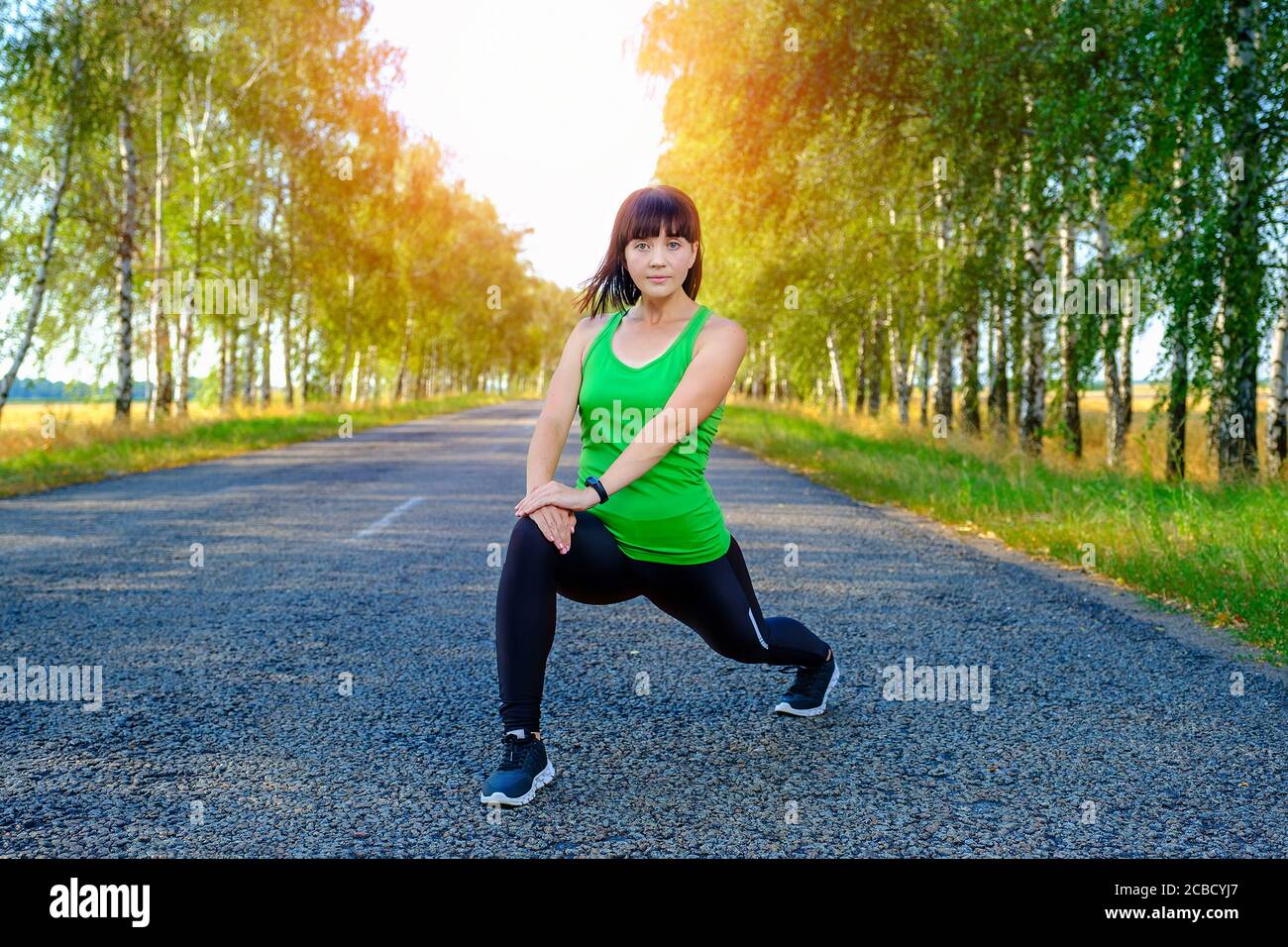 Jeune femme qui s'étire les jambes avant de courir sur la route asphaltée Banque D'Images