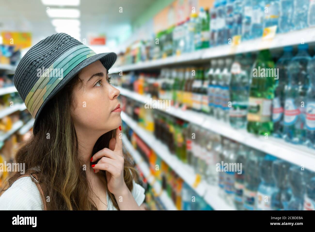 Une jeune femme choisit une bouteille d'eau dans le magasin. Concept de sélection de produits de supermarché. Banque D'Images