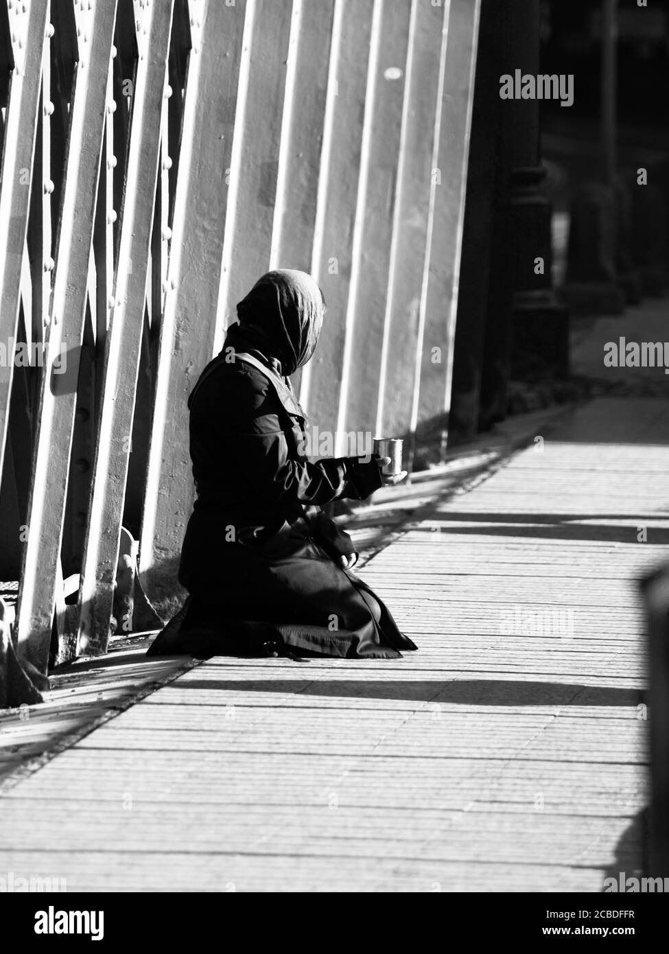 Femme musulmane vêtue de noir assise dans la rue et demandant des almes. Image en noir et blanc. Banque D'Images