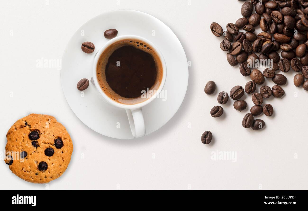 Grains de café torréfiés, biscuits aux pépites de chocolat et une tasse de café placés sur un fond blanc de plan d'examen. Banque D'Images