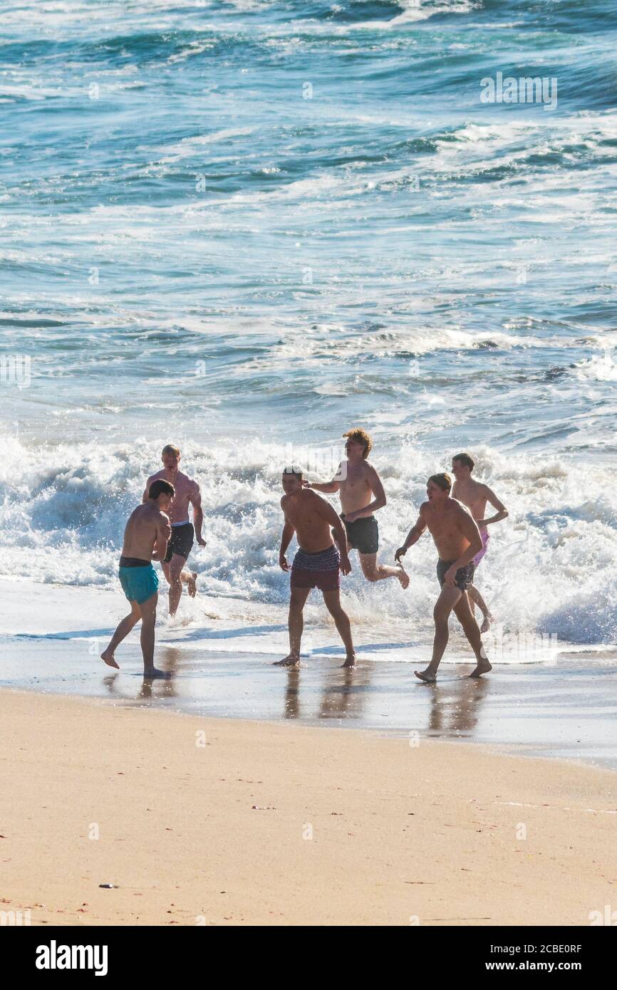 Des vacanciers masculins en vacances de vacances à pied hors de la mer à Fistral Beach à Newquay en Cornouailles. Banque D'Images