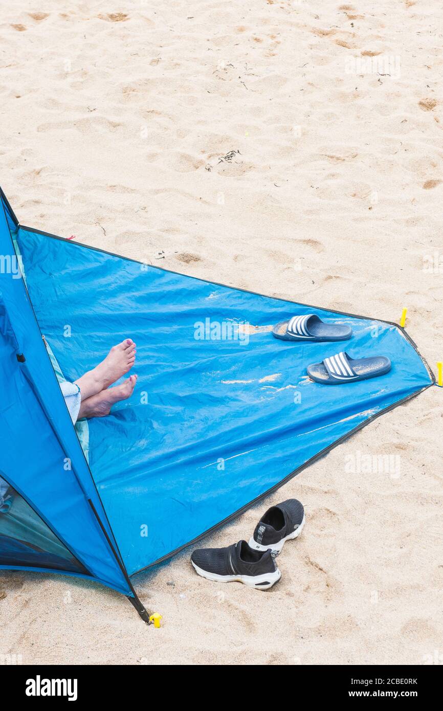 Un holidaymaker lors d'un séjour de vacances de vacances assis à l'intérieur d'un abri de plage bleu sur la plage de Fistral à Newquay en Cornouailles. Banque D'Images
