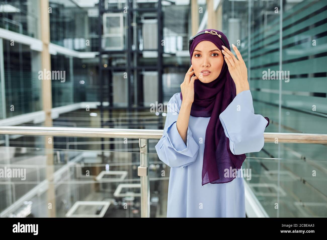 Portrait de mode de la belle jeune femme musulmane élégante portant le  violet hijab et robe en soie bleue à l'intérieur moderne de l'hôtel avec  beaucoup de verre Photo Stock - Alamy