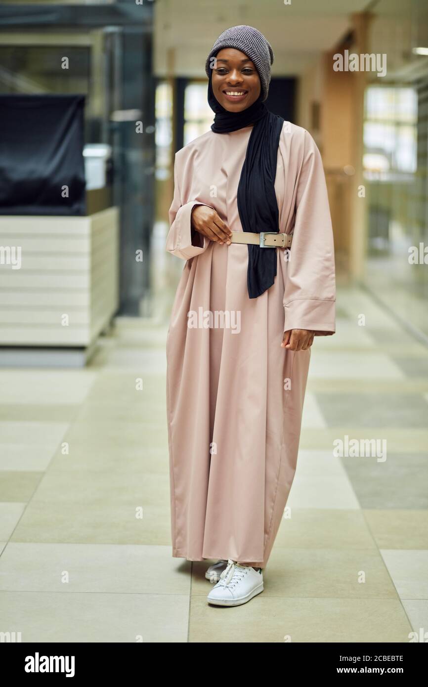 Jeune femme musulmane africaine à la mode joyeuse portant une robe longue  rose et un chapeau tricoté sur un foulard noir, scène urbaine Photo Stock -  Alamy