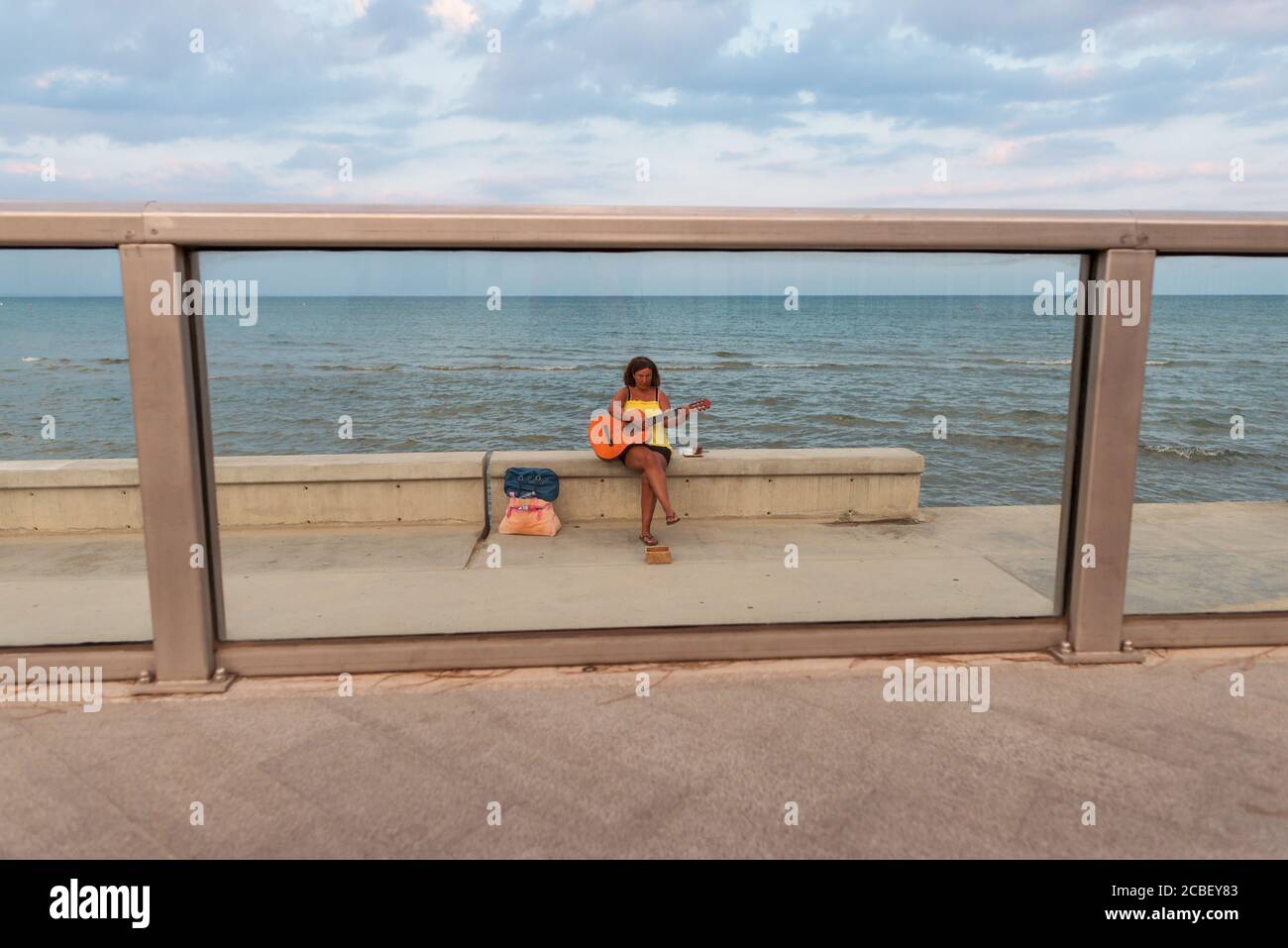 Larnaca / Chypre - 15 août 2019: Femme jouant de la guitare pour les alms assis sur le mur de la promenade avec la mer en arrière-plan Banque D'Images