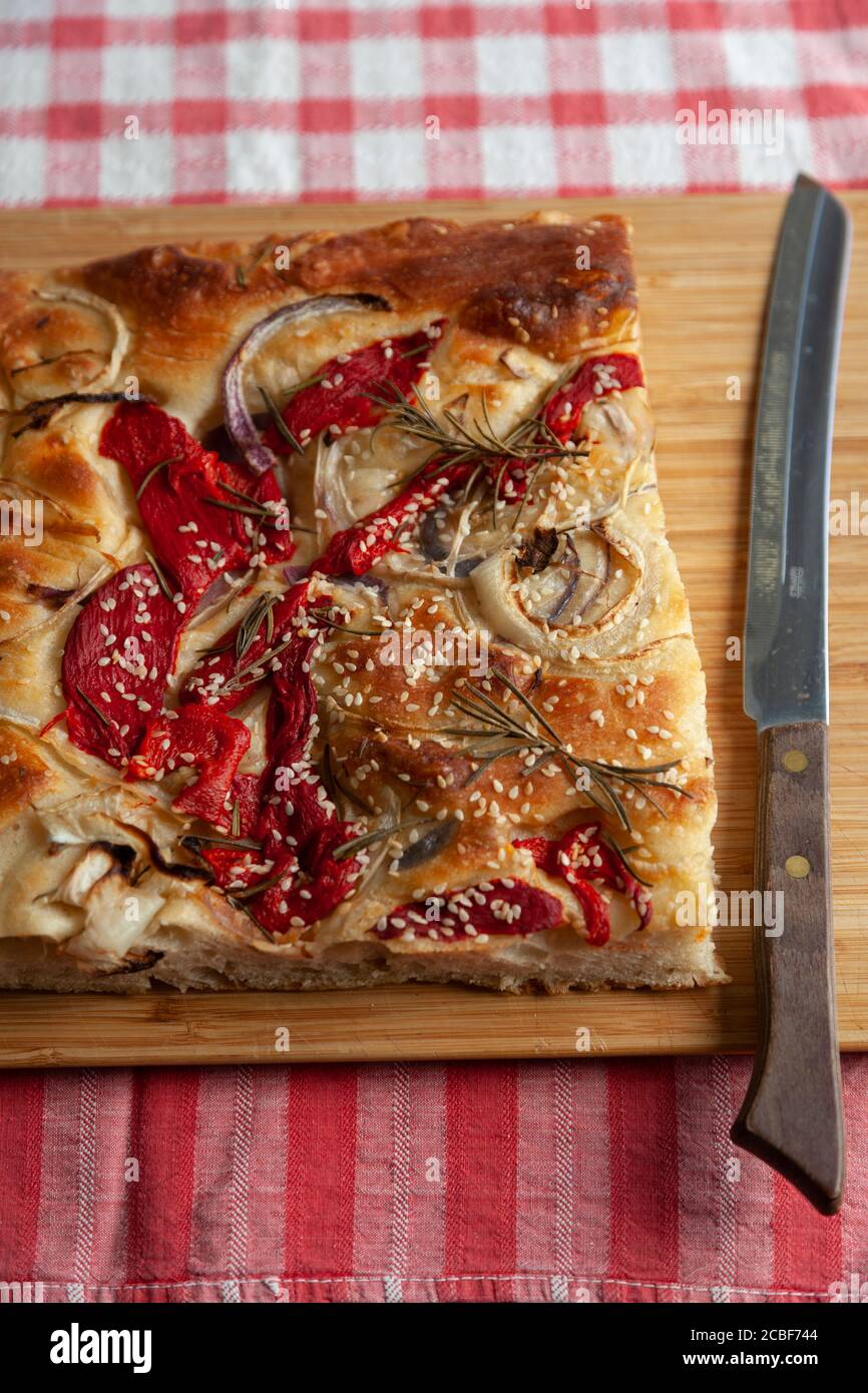 Un grand morceau de foccacia fraîchement cuit, recouvert de poivrons rouges, d'oignons, de graines de sésame et de romarin Banque D'Images