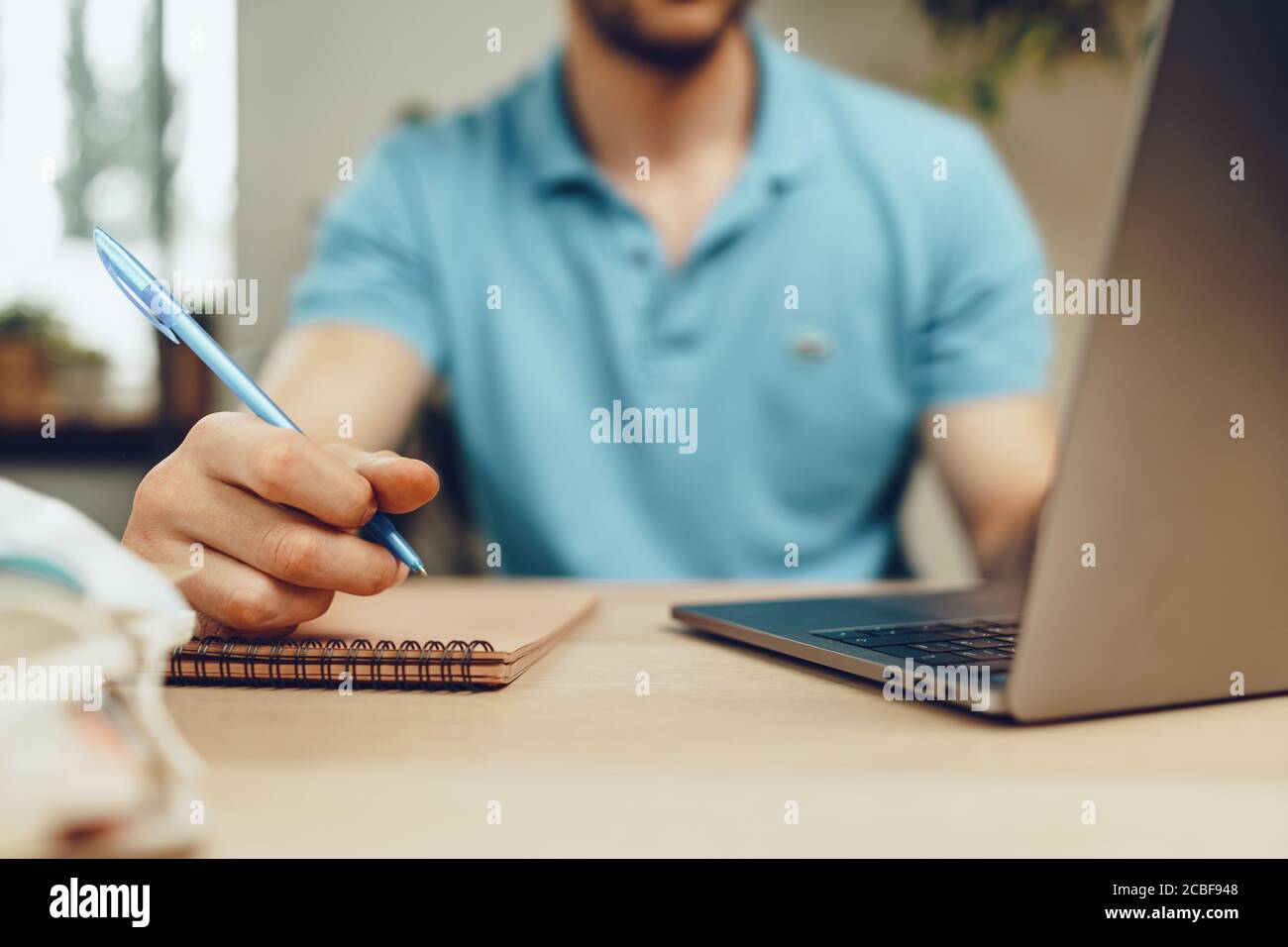 Des étudiants de sexe masculin font des études à domicile pendant la quarantaine. Gros plan d'une table avec un ordinateur portable, des carnets et un masque médical Banque D'Images