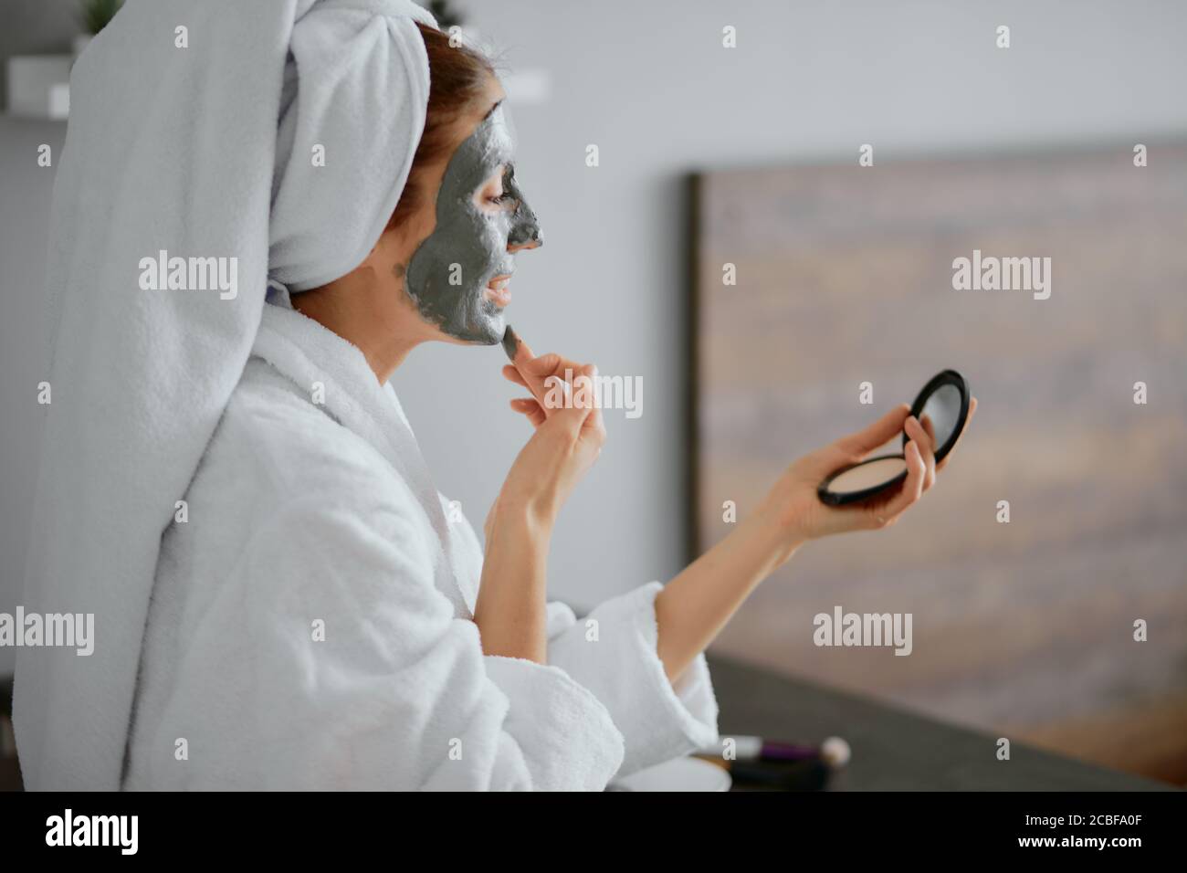 jeune femme caucasienne appliquant un masque facial portant un peignoir et une serviette dans la chambre, regardez l'appareil photo Banque D'Images