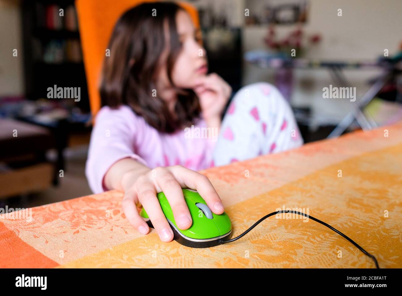 La fille contrôle la souris d'ordinateur. L'enfant est assis sur une chaise à la maison. Étudier à la maison. Banque D'Images