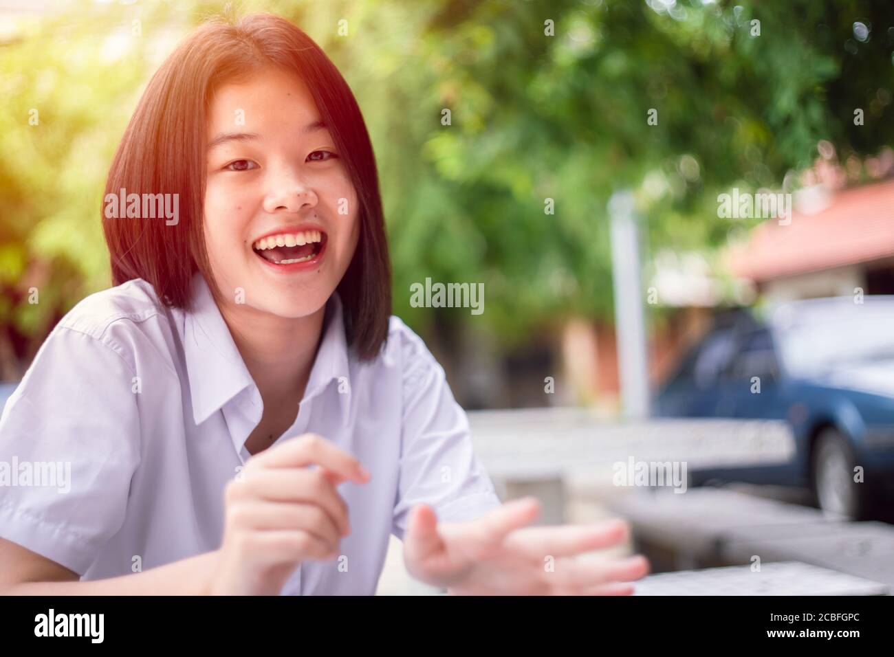 Joyeux sourire asiatique étudiant fille adolescent jeune mignon assis à l'extérieur regarder un appareil photo avec espace de copie Banque D'Images