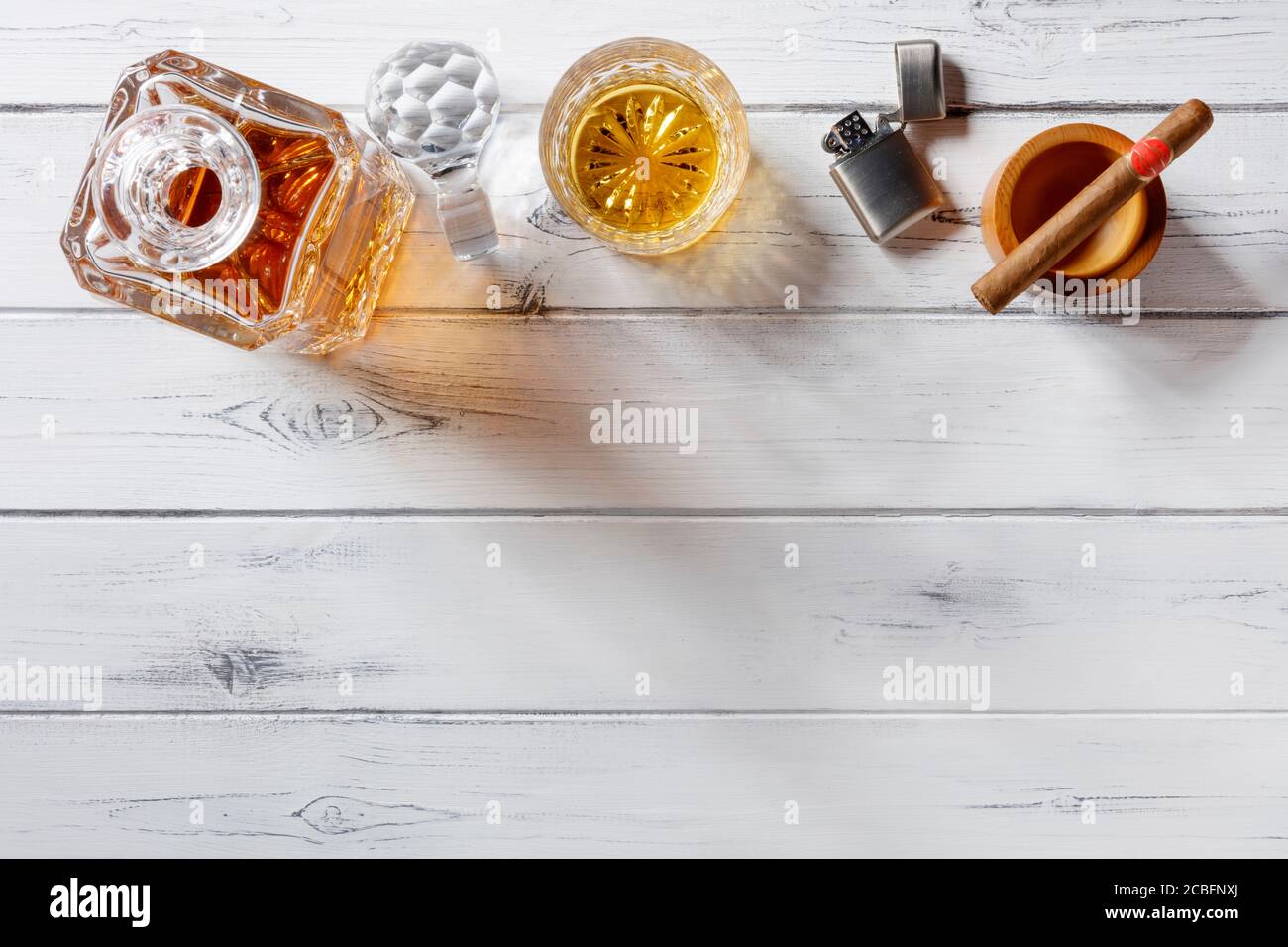 Vue d'un verre de cristal et d'un carafe rempli de whisky doré, d'un allume-cigare et d'un allume-cigare, tiré d'en haut sur un fond en bois blanc vieilli avec Banque D'Images