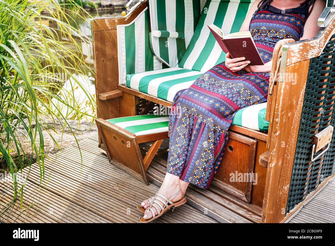 femme en robe d'été se détendant dans la chaise de plage sur la terrasse ou patio lisant un livre Banque D'Images