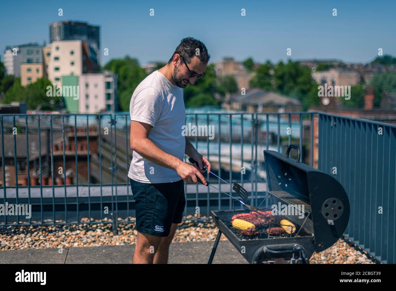 Homme cuisinant sur un barbecue, un steak argentin, des saucisses, de la viande et du maïs lors d'un barbecue par une chaude journée d'été Banque D'Images