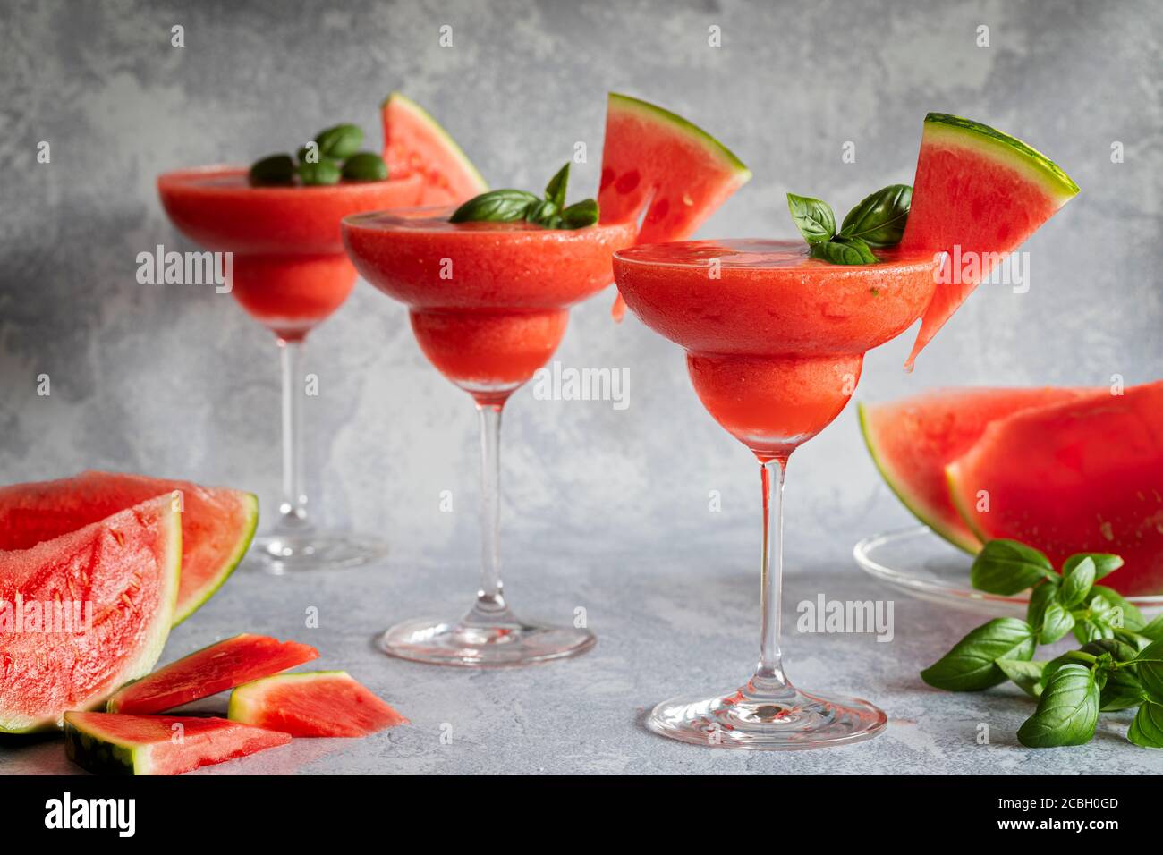Trois boissons frappées de margarita fraîches et congelées, accompagnées de fraises et de pastèques. Les boissons sont garnies de feuilles de basilic et de pastèque. Fond gris Banque D'Images