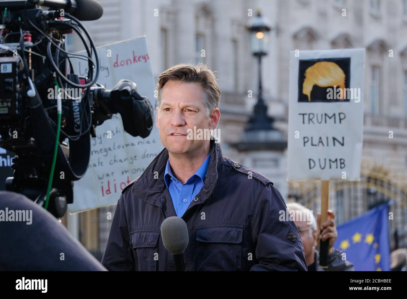 Un correspondant de nouvelles rapporte en direct pendant la visite d'État de Donald Trump au Royaume-Uni le 3 juin. Des manifestants avec des pancartes anti-Trump se tiennent devant la caméra. Banque D'Images