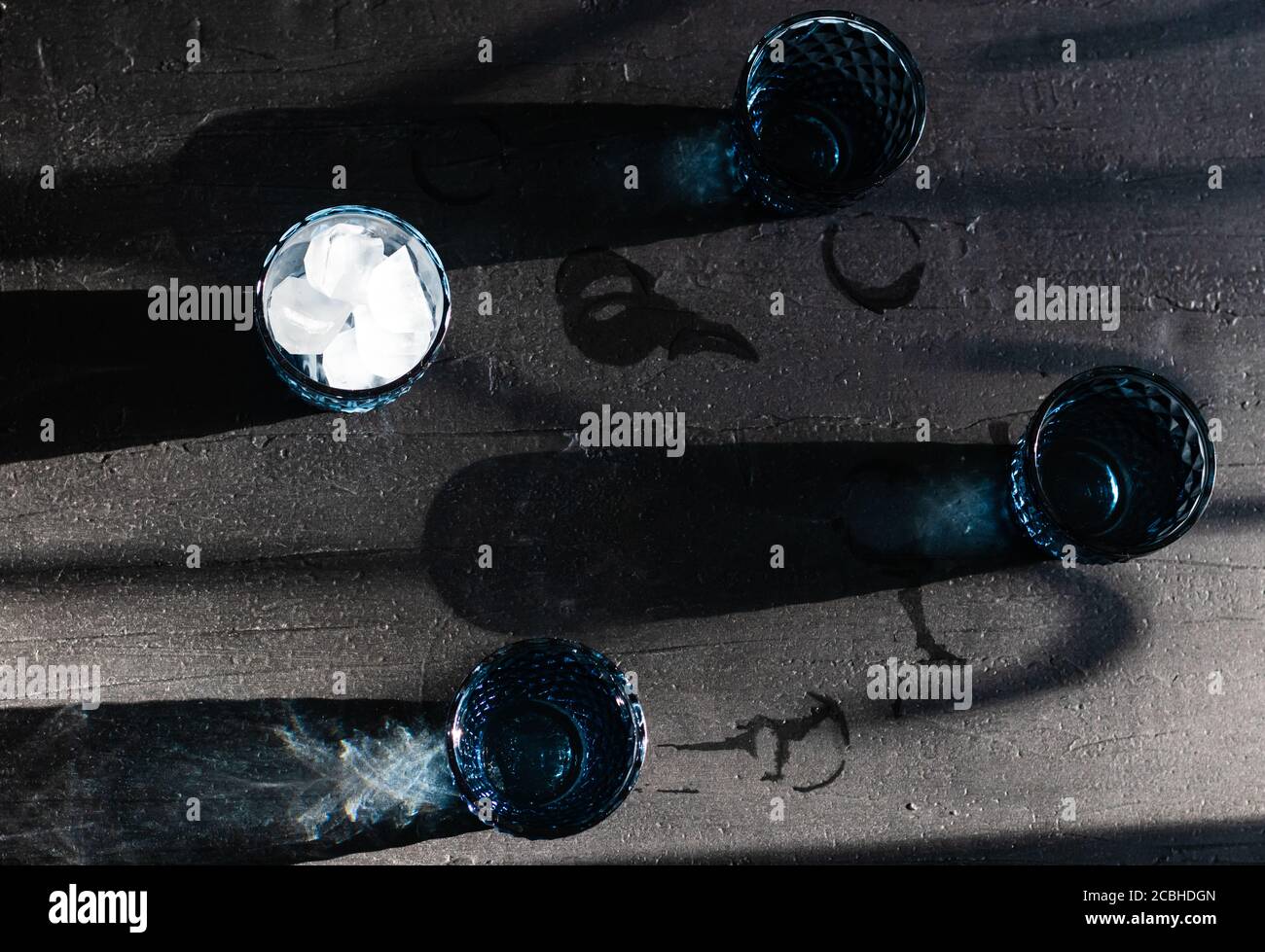 Verres à boisson bleus avec eau et glace et longues ombres de couleur sur un fond noir texturé. Vue de dessus Banque D'Images