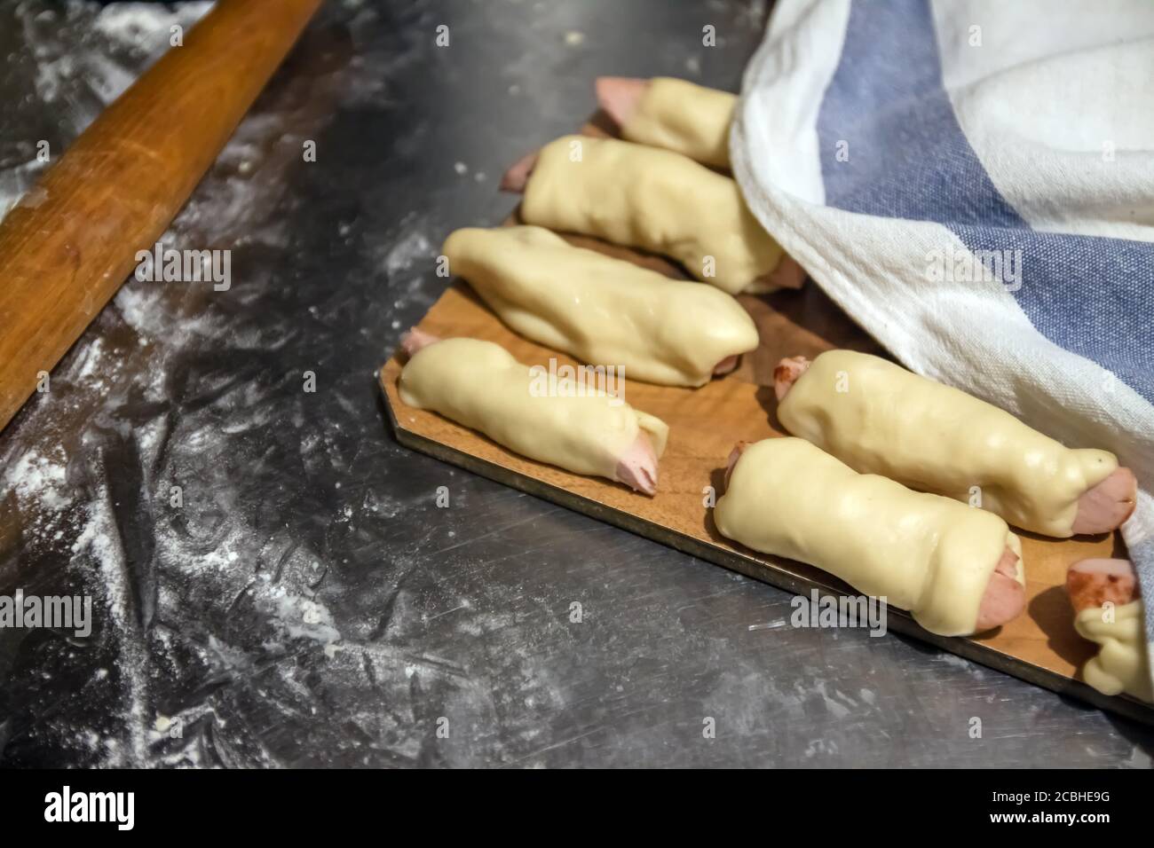 Les saucisses crues préparées dans le test avant la cuisson se trouvent sur une table sous une serviette. Concept, cuisine maison Banque D'Images