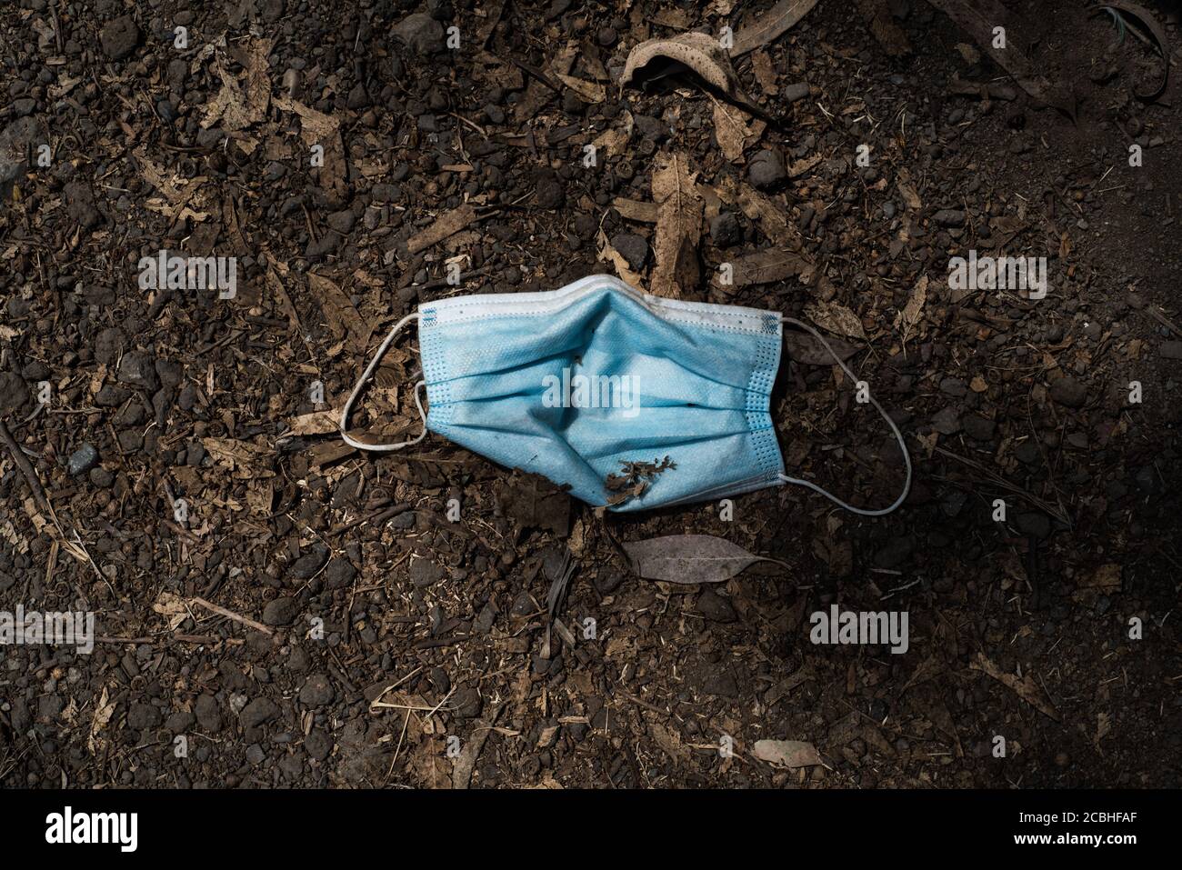 Un masque jetable bleu trouvé dans la rue. Vue de dessus du masque médical en contour d'oreille jeté ou perdu sur sol brun pendant la pandémie COVID-19. Banque D'Images