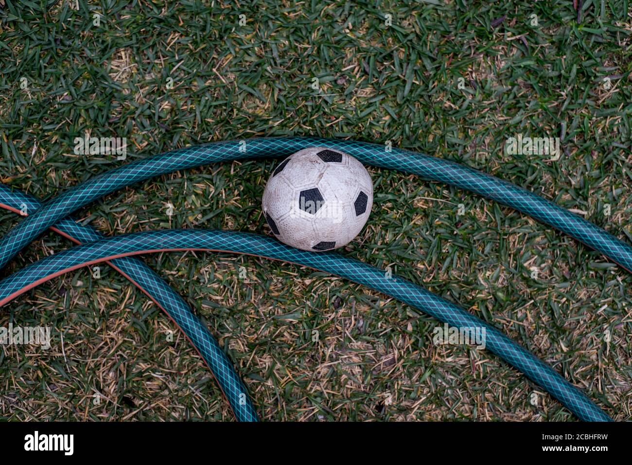 Vue de dessus d'un ballon de football noir et blanc sale à côté d'un tuyau vert dans un jardin formant une forme intéressante. Banque D'Images